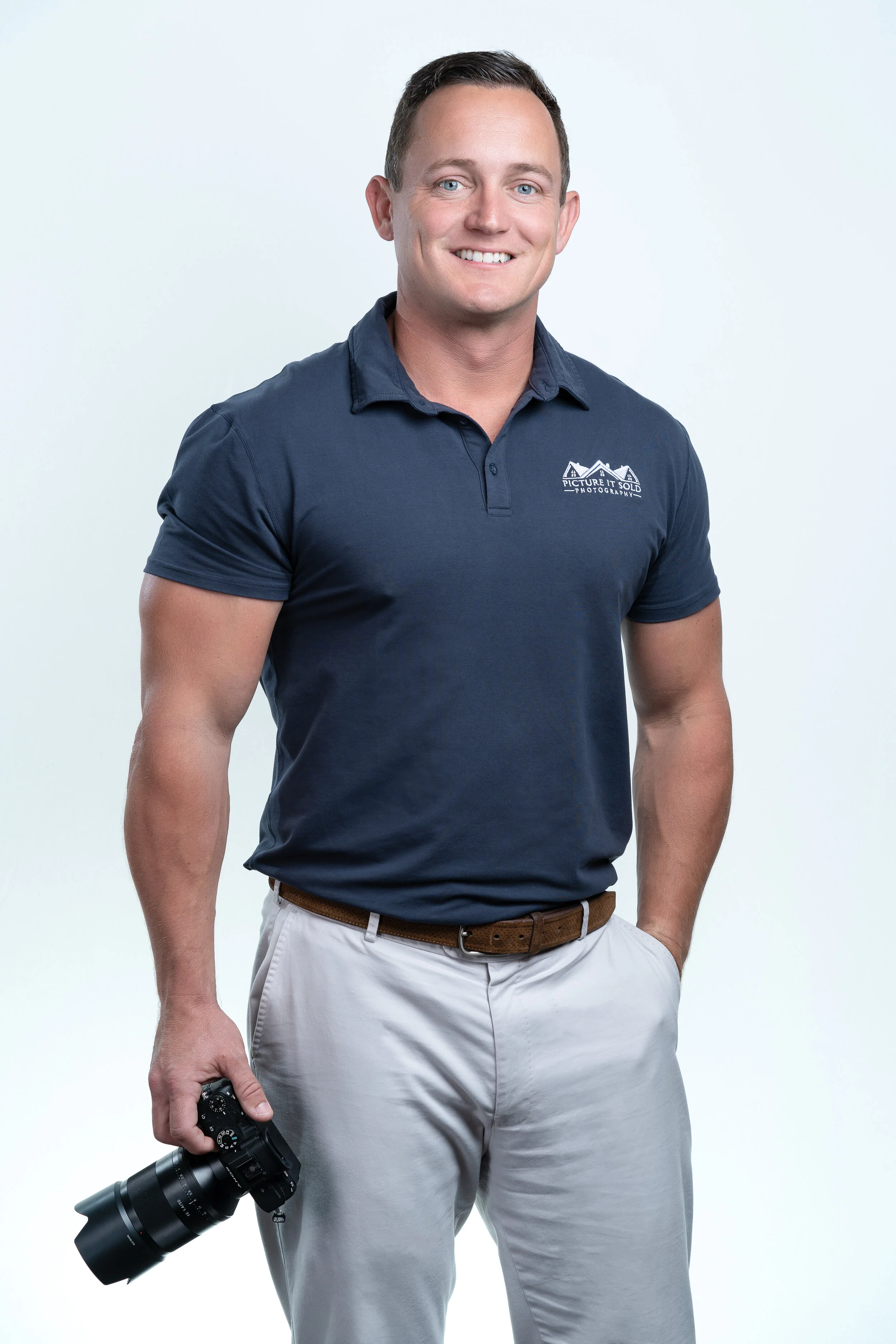 Man in a navy polo shirt holding a camera against a plain background.