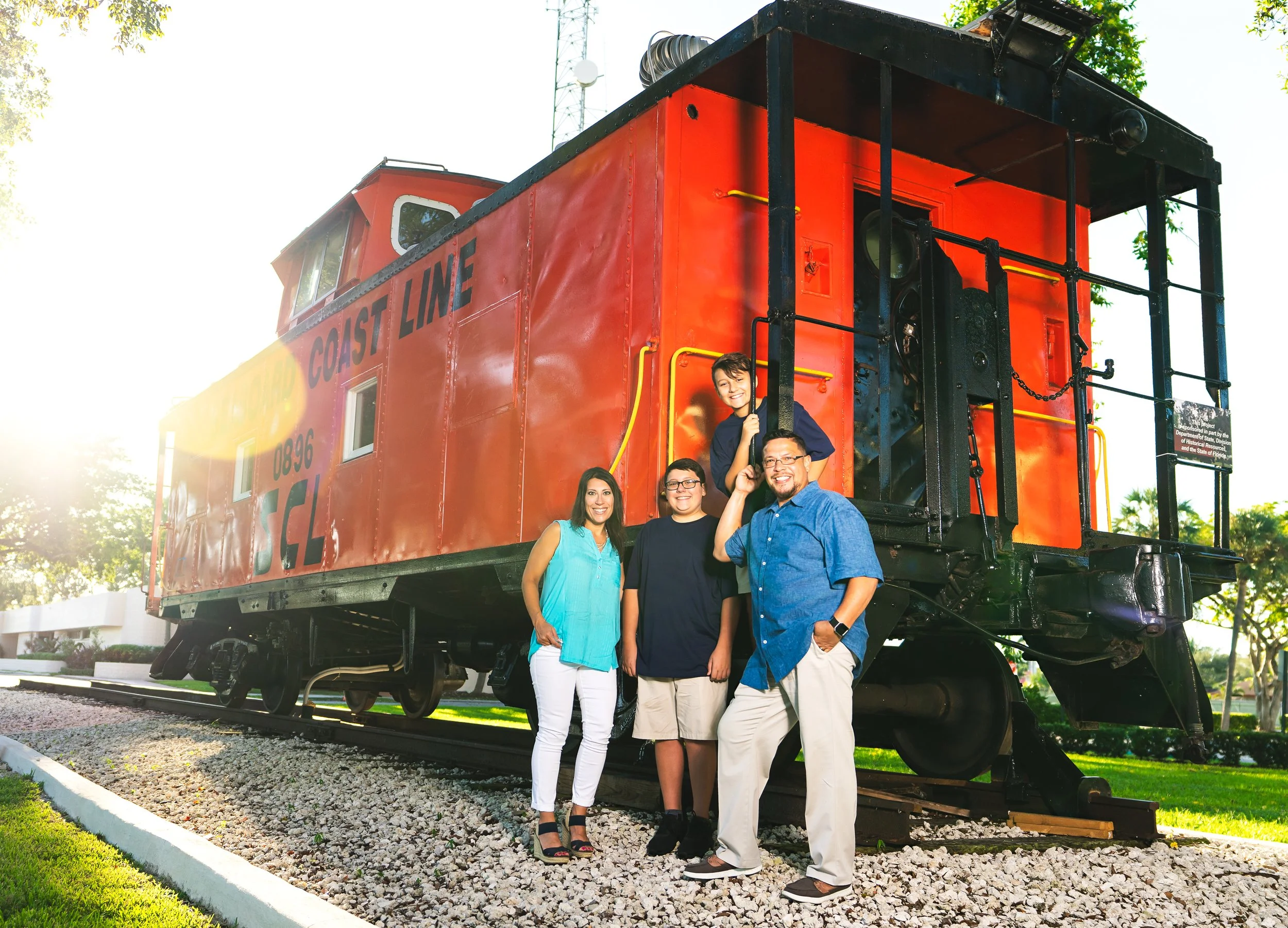 Family posing in front of a vintage red caboose train labeled 'Coast Line' in a park setting.