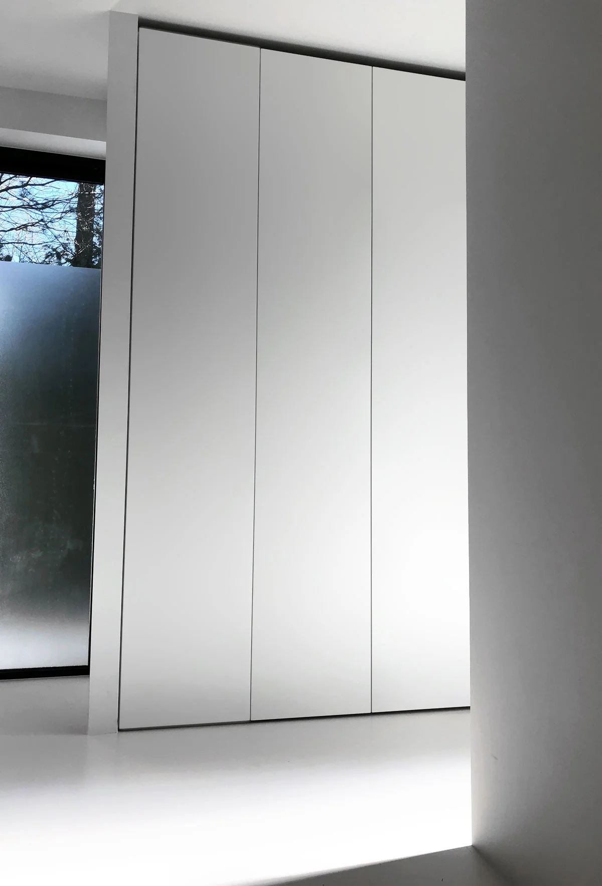 Afbeelding van een minimalistische design kledingkast op maat met handgreeploze deuren van vloer tot plafond.