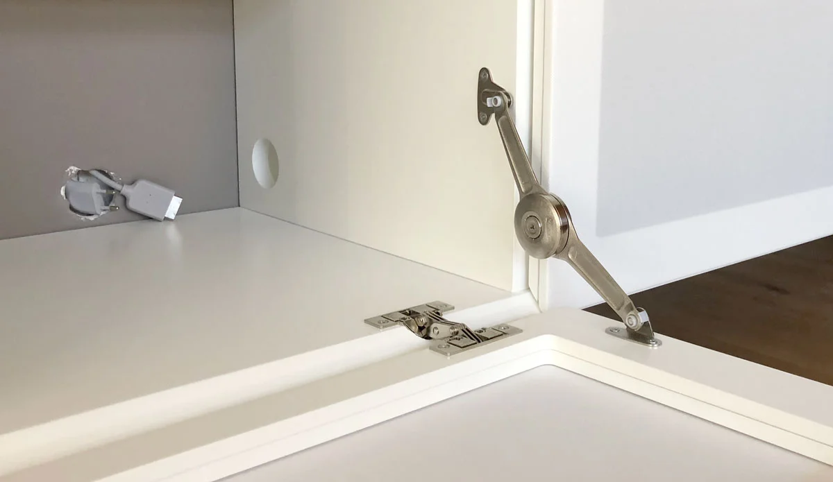 Detailafbeelding van een verstekscharnier, klephouder en kabels uit de muur in een wit TV meubel.