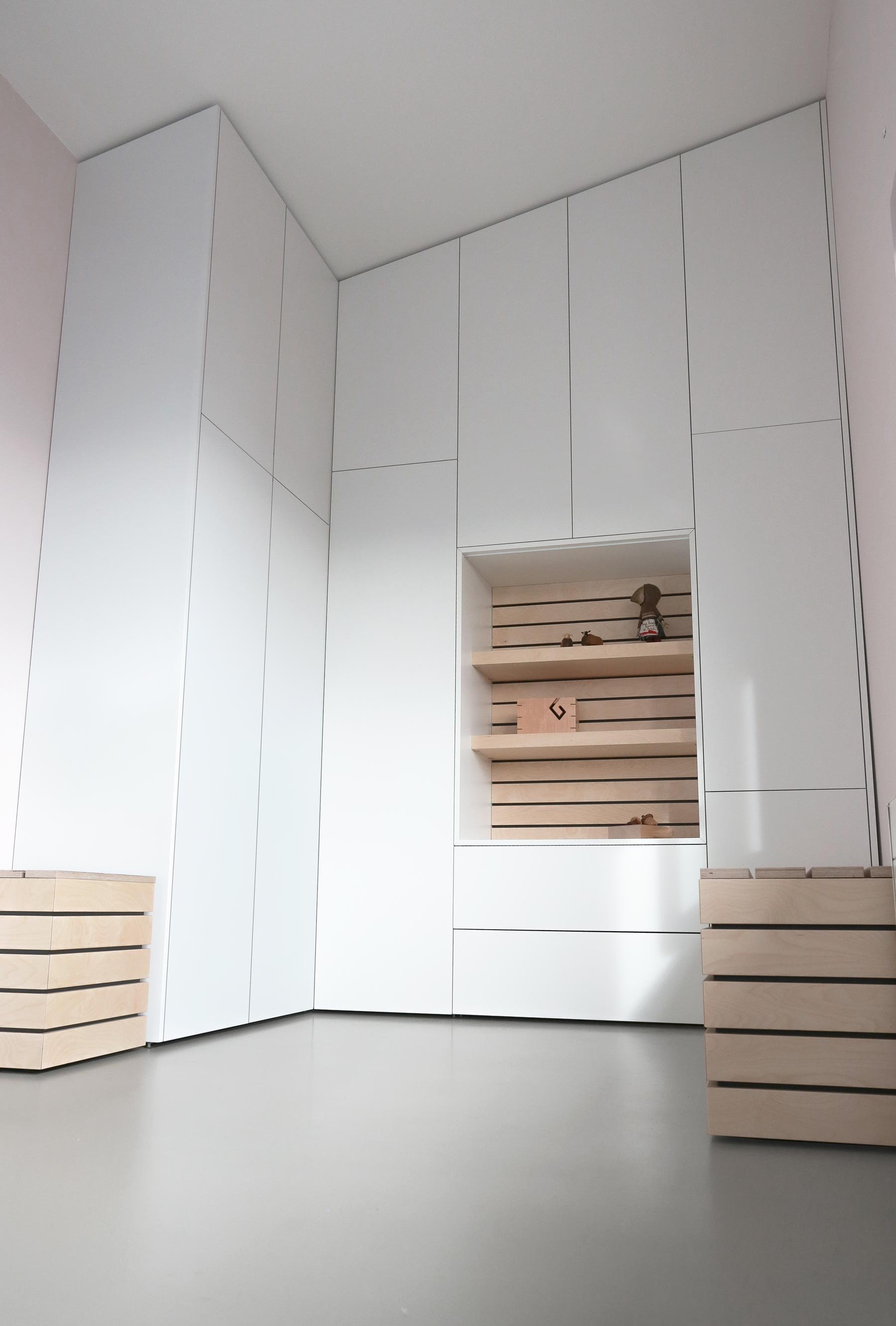 Witte inbouwkast op maat onder schuin plafond in multifunctionele kamer met open vak en houten details