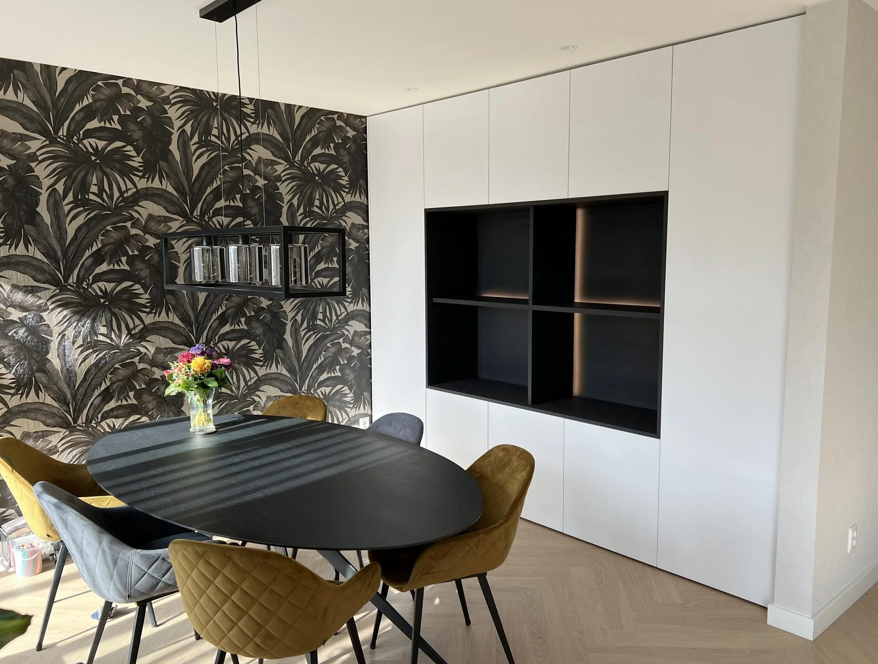 Witte kastenwand in nis met groot donker open vak en ledverlichting, gezien vanuit de eetruimte