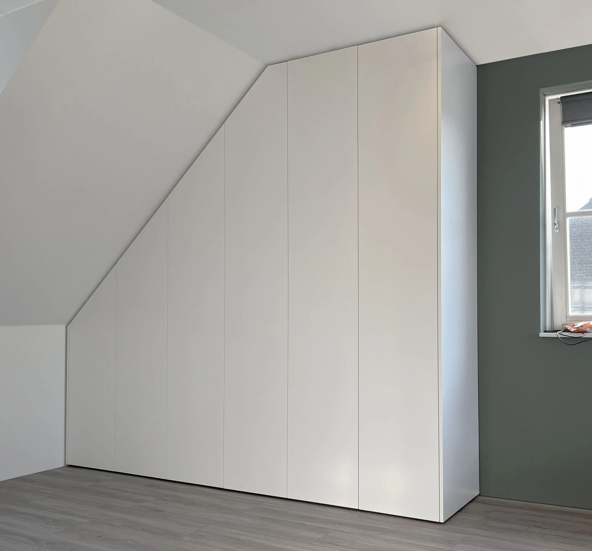 Witte kastenwand op maat onder schuin plafond met verfijnde schaduwvoeg rondom