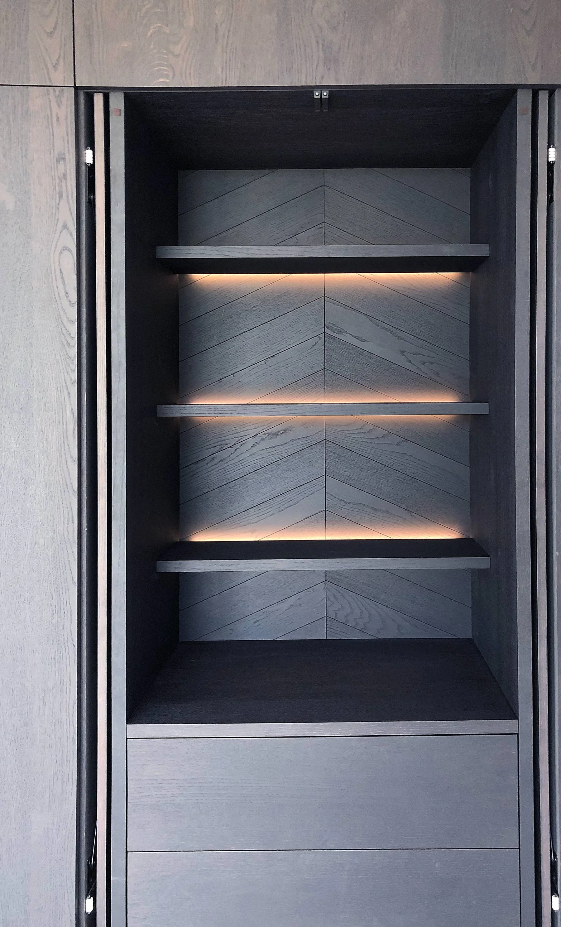 Detail van open vak met visgraat achterwand en ledverlichting in zwart gebeitst eiken fineer