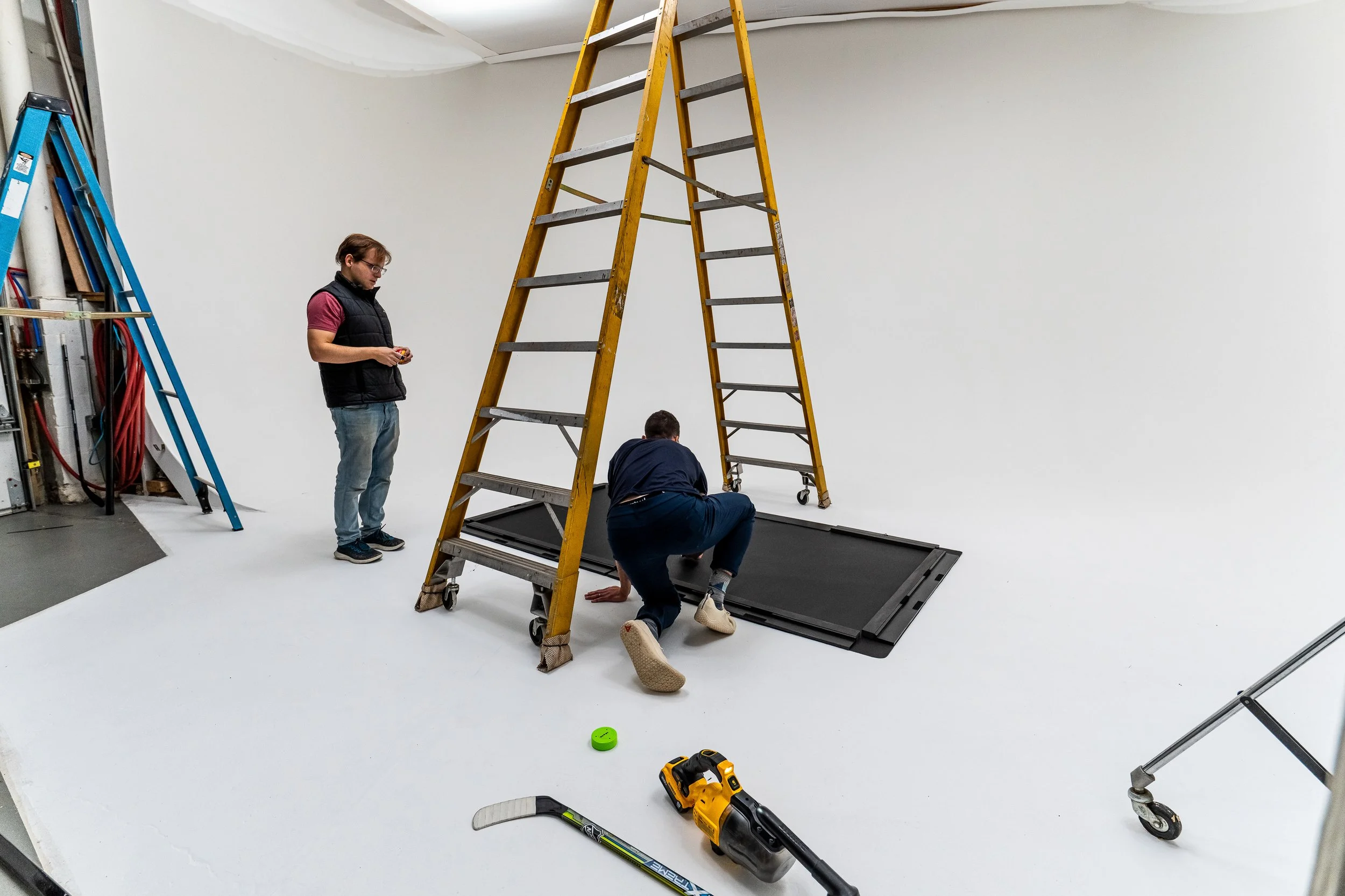 Behind the scenes view of a commercial and industrial product photoshoot with ladders, crew, and a hockey training mat on a white cyclorama in Pittsburgh PA, photographed by Ian Jones of ISJDESIGNS
