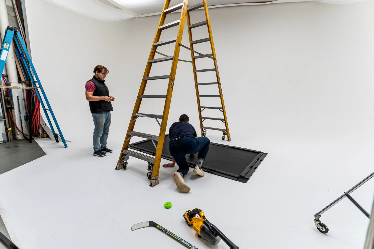 Behind the scenes view of a commercial and industrial product photoshoot with ladders, crew, and a hockey training mat on a white cyclorama in Pittsburgh PA, photographed by Ian Jones of ISJDESIGNS