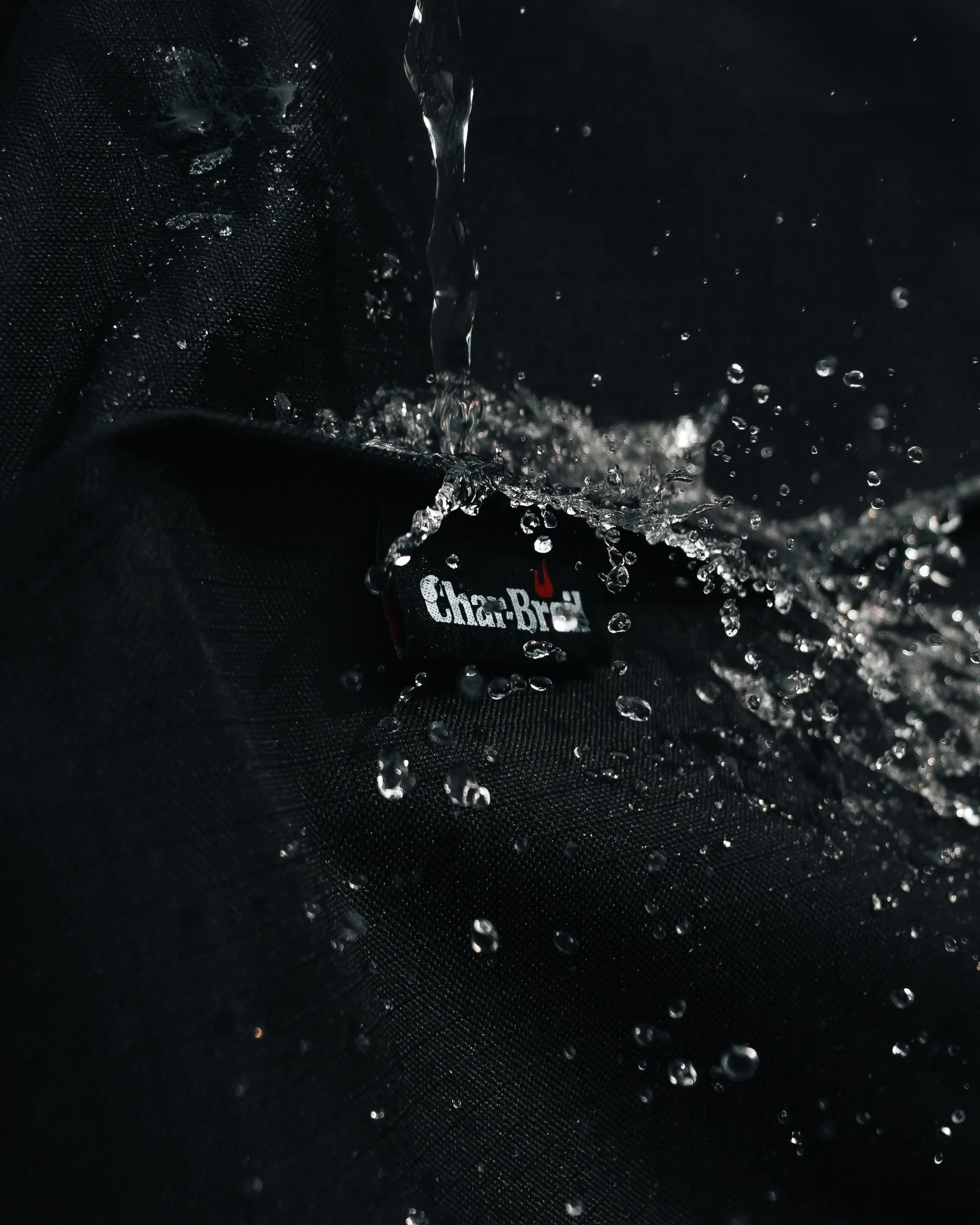 Cinematic macro product photo of a Char-Broil grill cover with water splashing over the logo — creative UGC brand photography by Ian Jones of ISJDESIGNS Pittsburgh