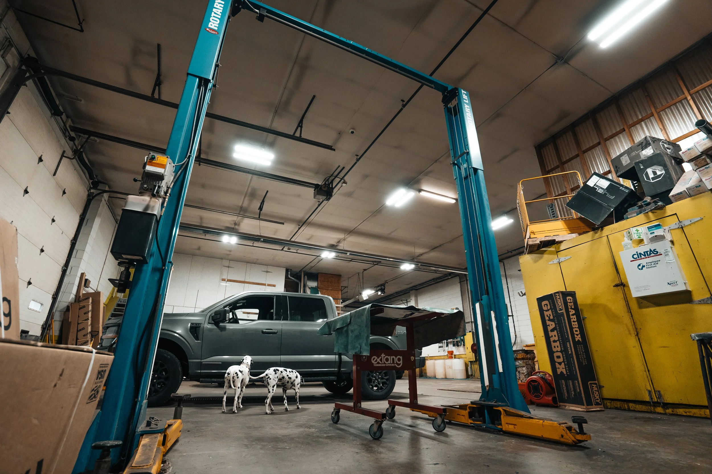 Industrial automotive garage scene in Pittsburgh showing a Rotary Lift, pickup truck, tool carts, and two dalmatians