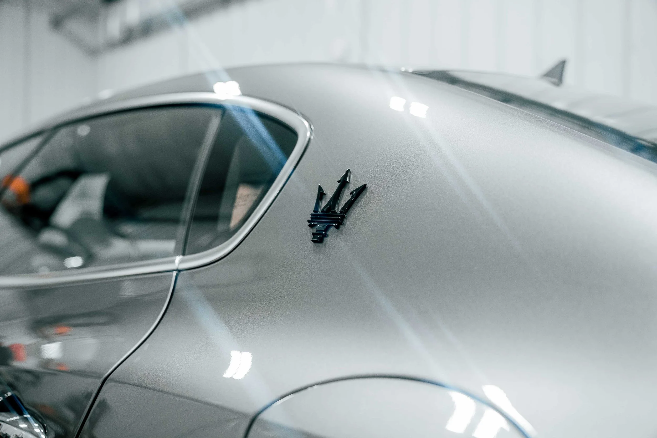 Close-up automotive photography of a silver Maserati Ghibli Q4 rear quarter panel and trident badge inside a Bridgeville, PA shop