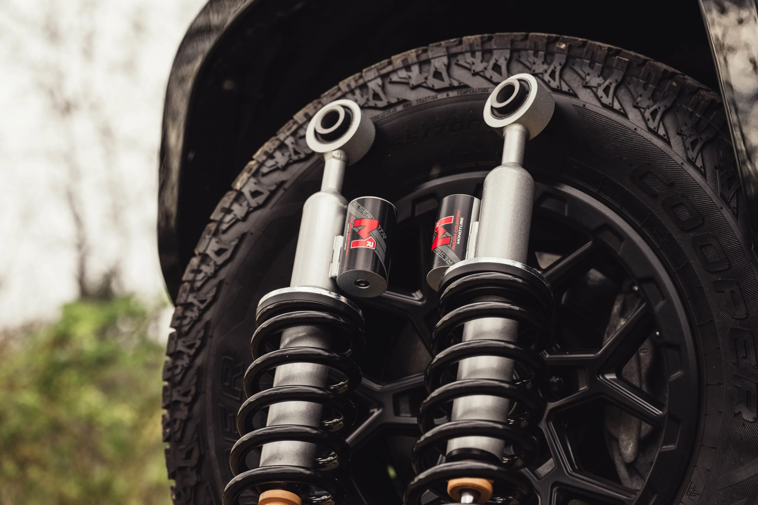 Rough Country M1R reservoir struts posed in front of a Cooper AT tire and RockTrix RT107 wheel on a 2025 Toyota 4Runner TRD Sport.