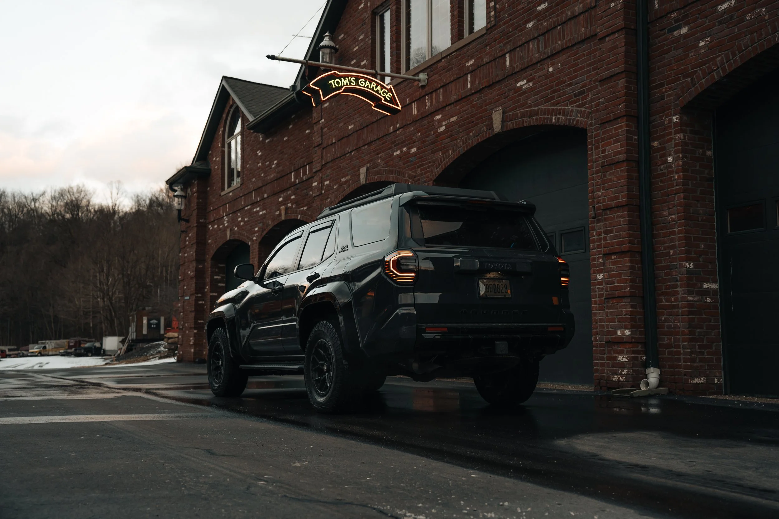 2025 Toyota 4Runner TRD Sport parked by a vintage brick garage with a glowing “Tom’s Garage” neon sign, taillights on say taken by Ian jones of isjdesigns in pittsburgh, PA