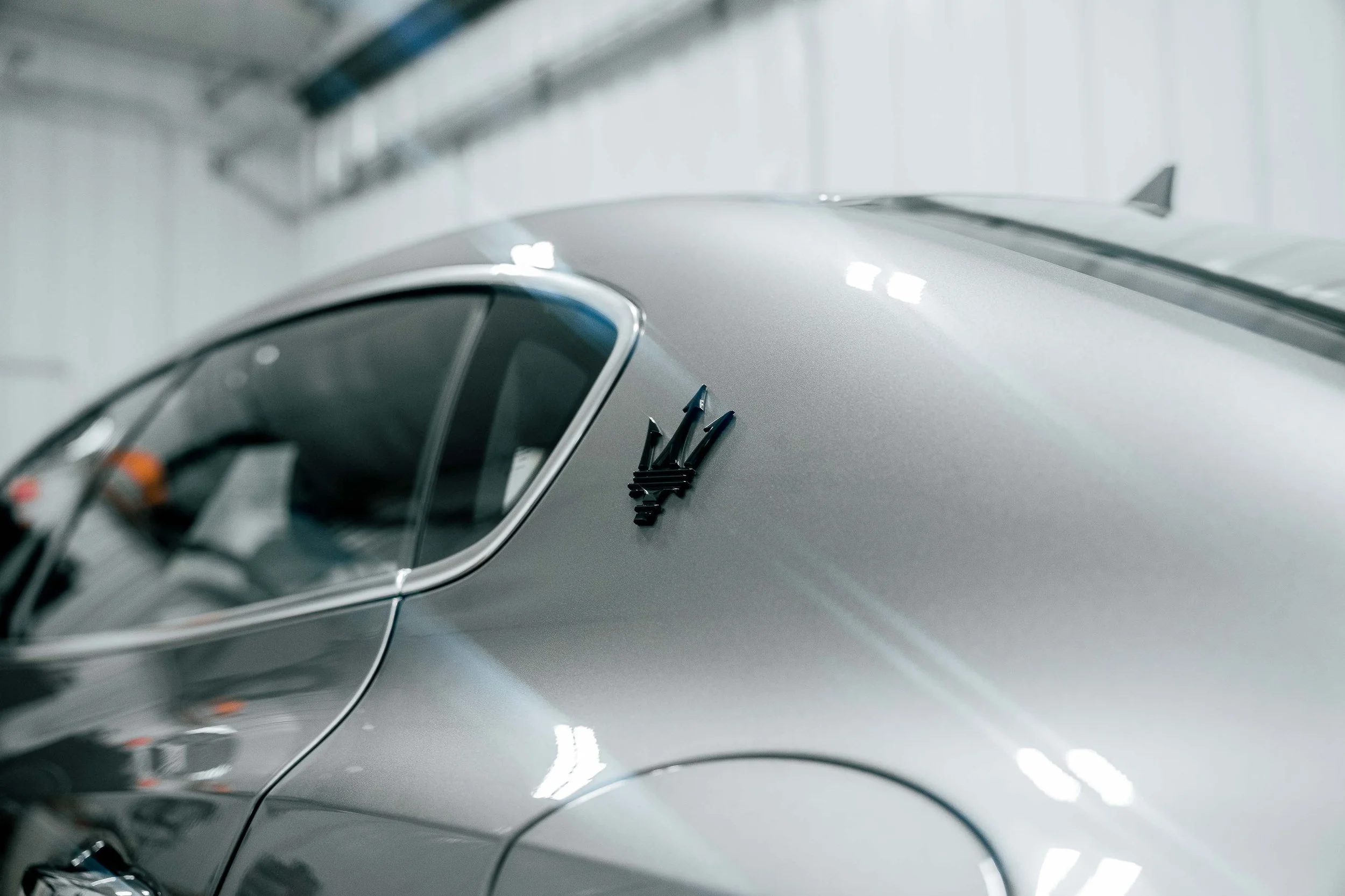 Automotive detail photography of a silver Maserati Ghibli Q4 trident emblem and rear quarter panel in Bridgeville, PA