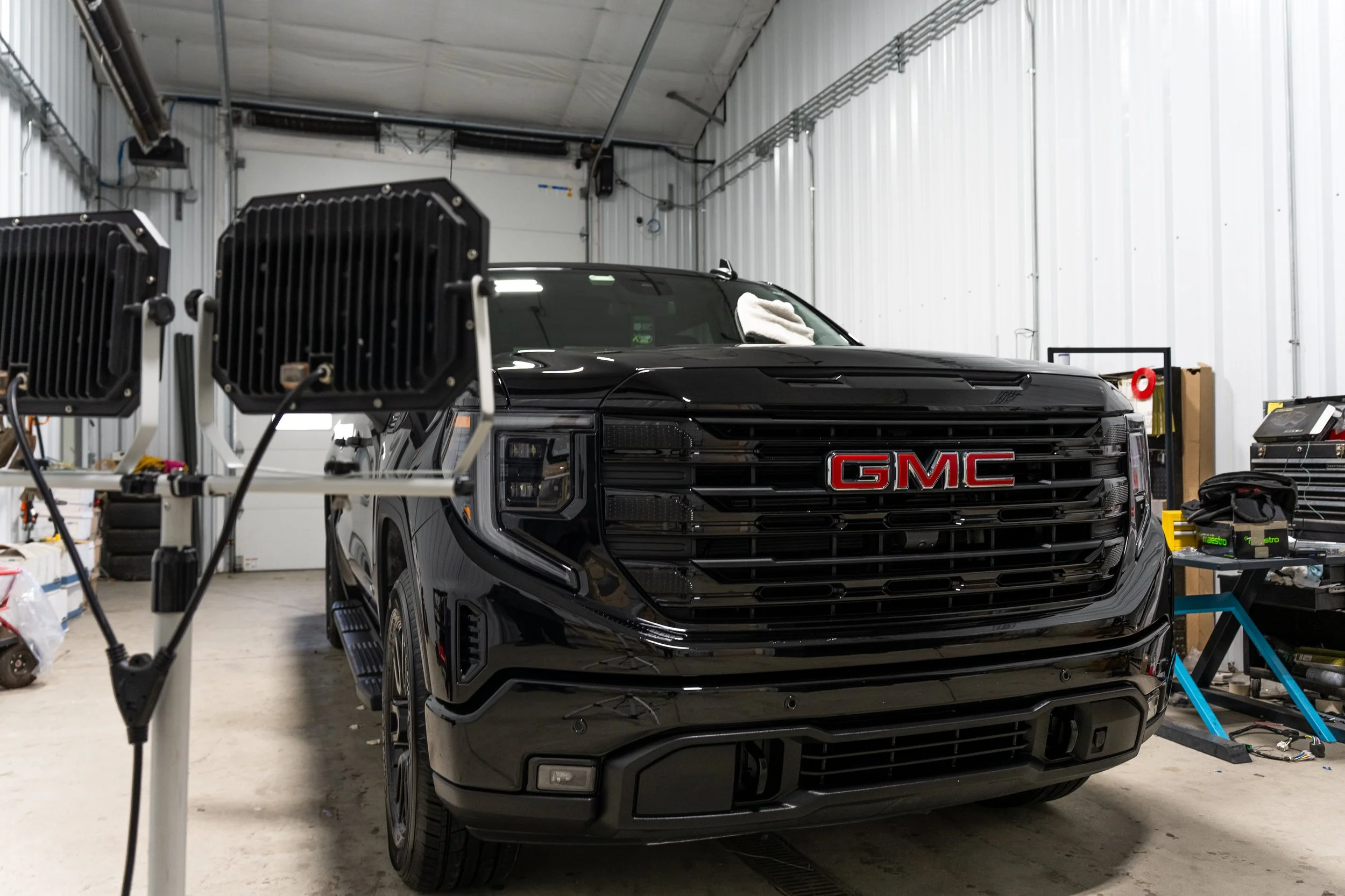 Professional automotive photo of a black GMC Sierra photographed head-on in a detail bay with clean, even shop lighting and glossy reflections.