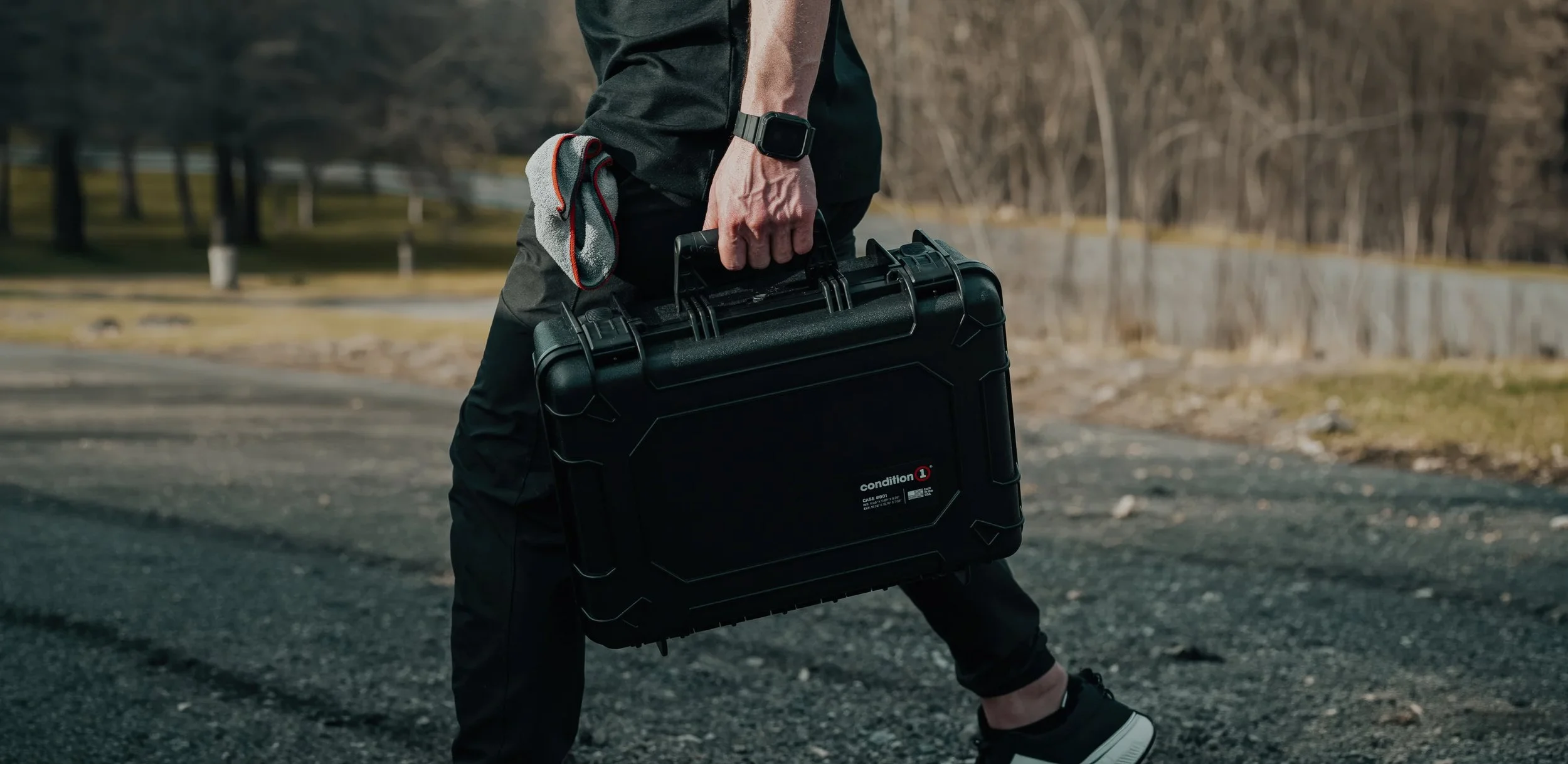 Man carrying a Condition 1 Case 801 protective hard case outdoors on a gravel path, lifestyle product photography by Ian Jones for Condition 1.