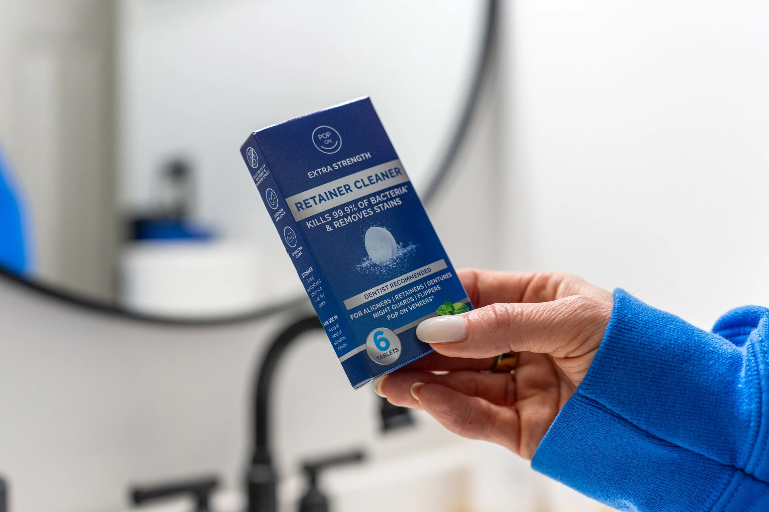 Hand holding Pop ON Extra Strength Retainer Cleaner box in a bright bathroom lifestyle product photo