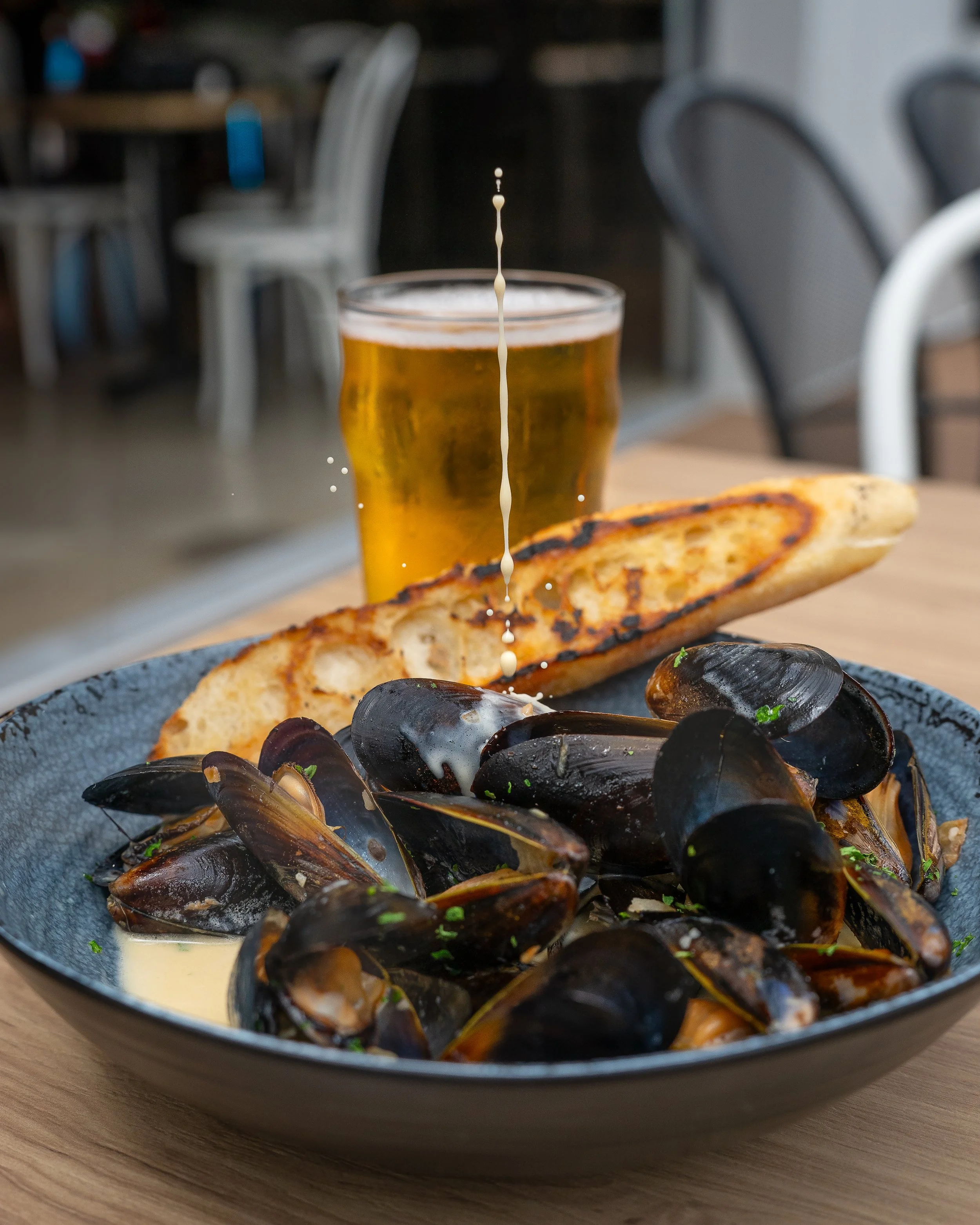 Mussels in white wine cream sauce with charred bread and a beer pour caught mid-stream, photographed with the Tamron 35-150mm f/2-2.8 on a Sony a1 in a Pittsburgh restaurant.