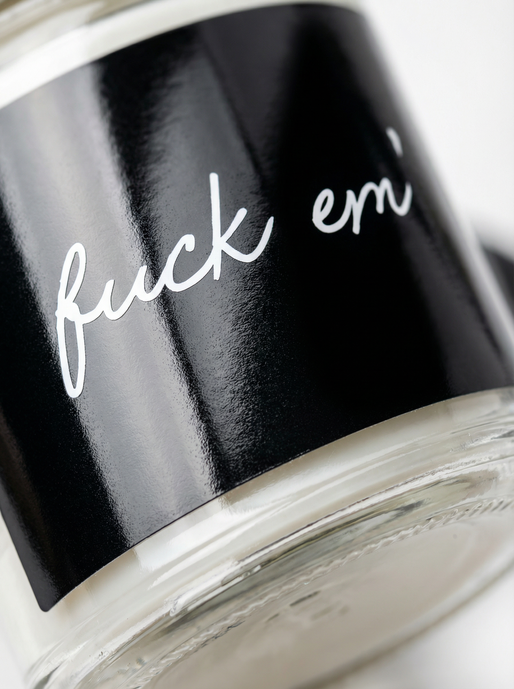 Macro close-up of the “Fuck Em” soy candle label on a clear glass jar. Bold black label with white script—perfect for novelty gift candle listings and product detail pages.