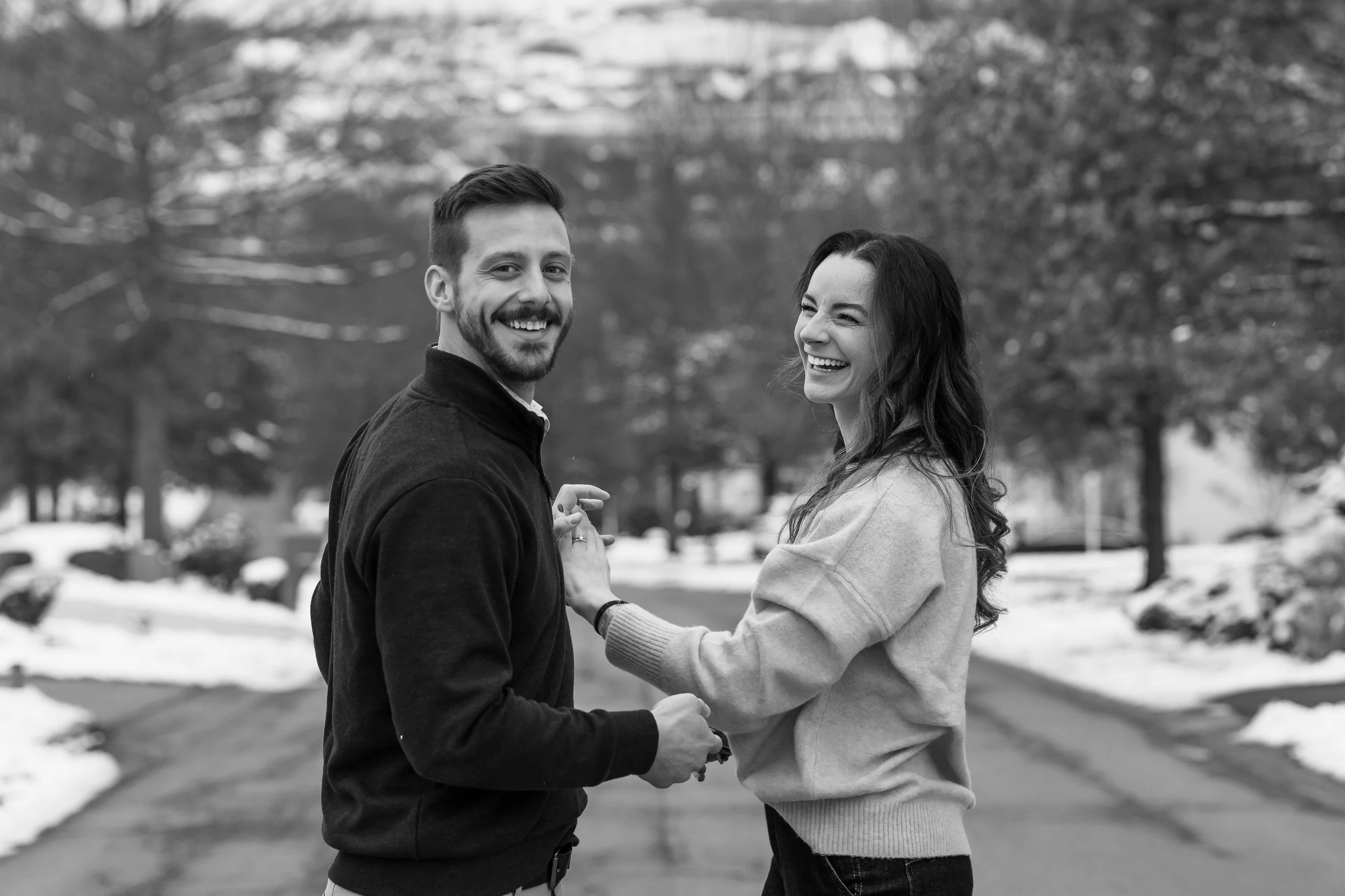 Candid black and white photo of a couple laughing together while walking down a snowy street in Washington Pennsylvania, photographed by Ian Jones of ISJDESIGNS
