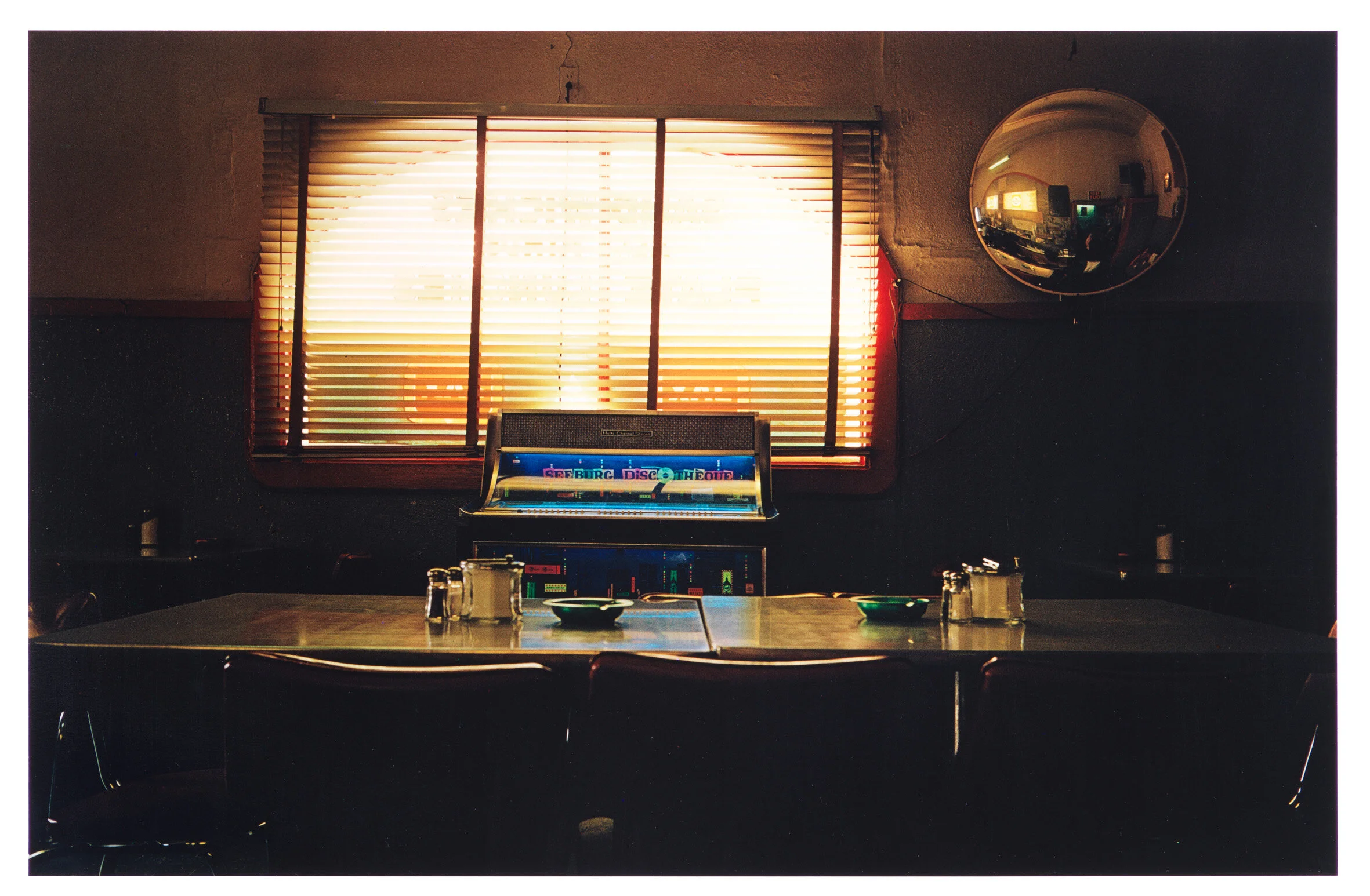 TABLE AND JUKEBOX  Dye-transfer. 1980. Signed and stamped on the verso. From the portfolio ‘Troubled Waters’ published in 1980 by Caldecot Chubb, New York. 290 x 443 mm (408 x 505 mm)