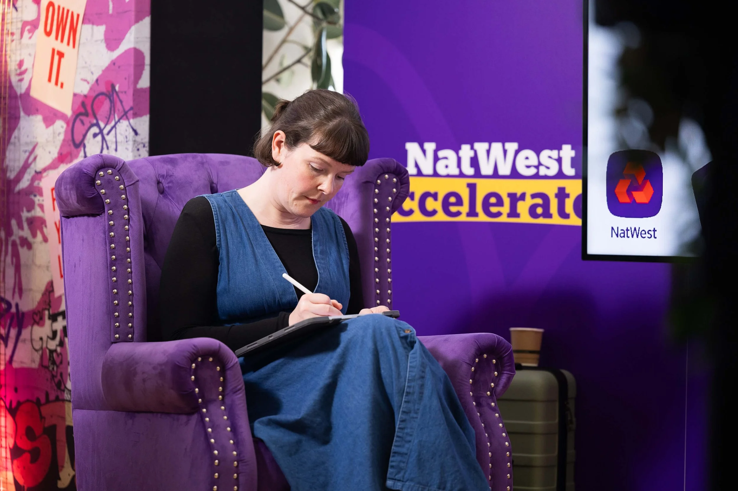 Close-up of Katie Chappell drawing on a tablet with a stylus in a purple armchair at the NatWest Accelerator, Oxford.