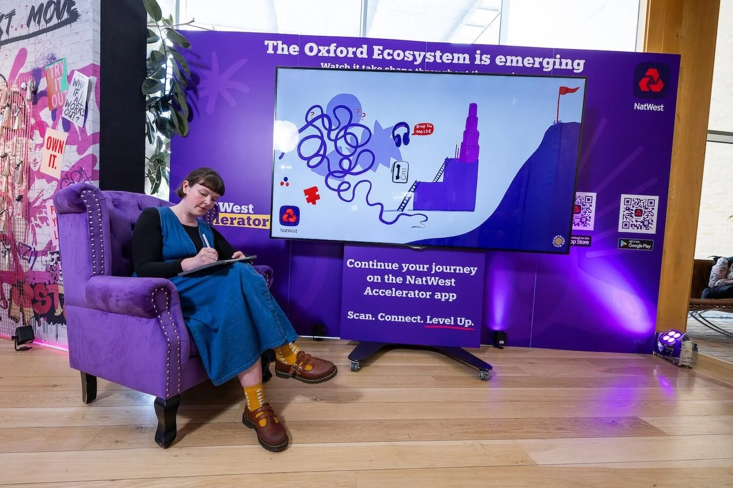 Live illustrator Katie Chappell drawing on a tablet beside a giant screen showing the early NatWest Accelerator artwork.