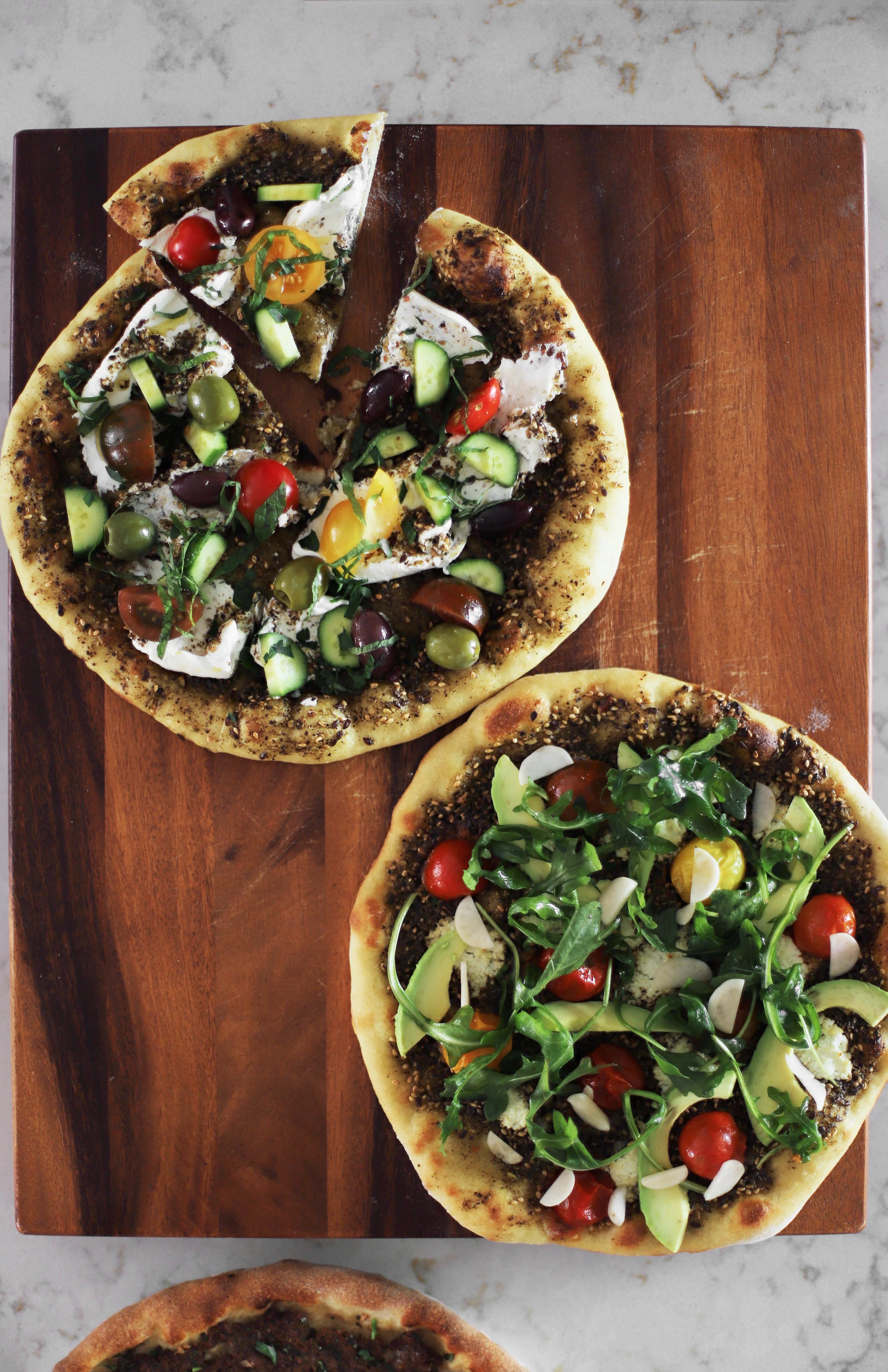 above: classic manakish with olives, tomatoes, cucumbers, labneh, and mint chiffonade below: california-style manakish with goat cheese, blistered tomato, arugula, avocado, pickled radishes or onions, and a little more extra virgin olive oil.