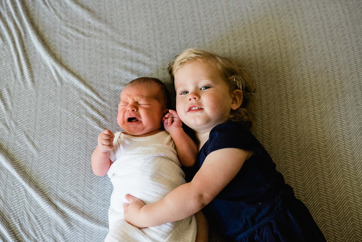 lifestyle newborn photographer in Fort Drum, NY - baby brother crying, big sister hugging.jpg
