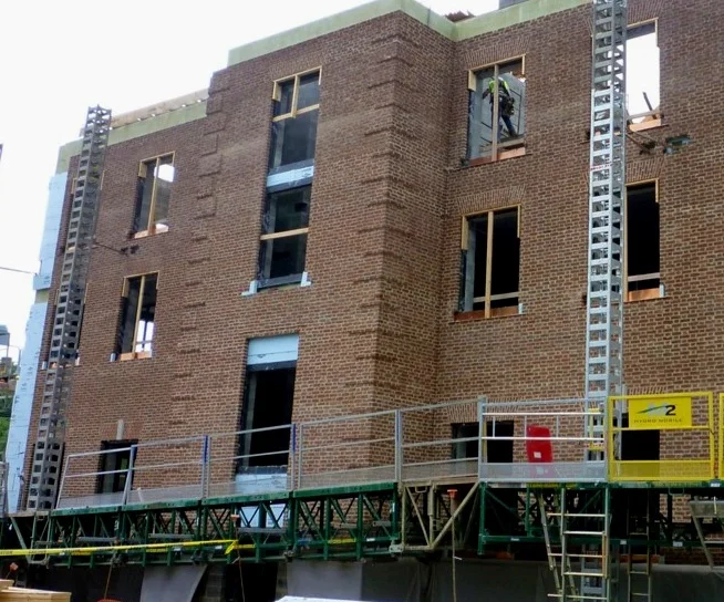 Hydro Mobile M2 Mast Climber - Masons using extended outriggers and walk-boards to reach wall with bump-out.