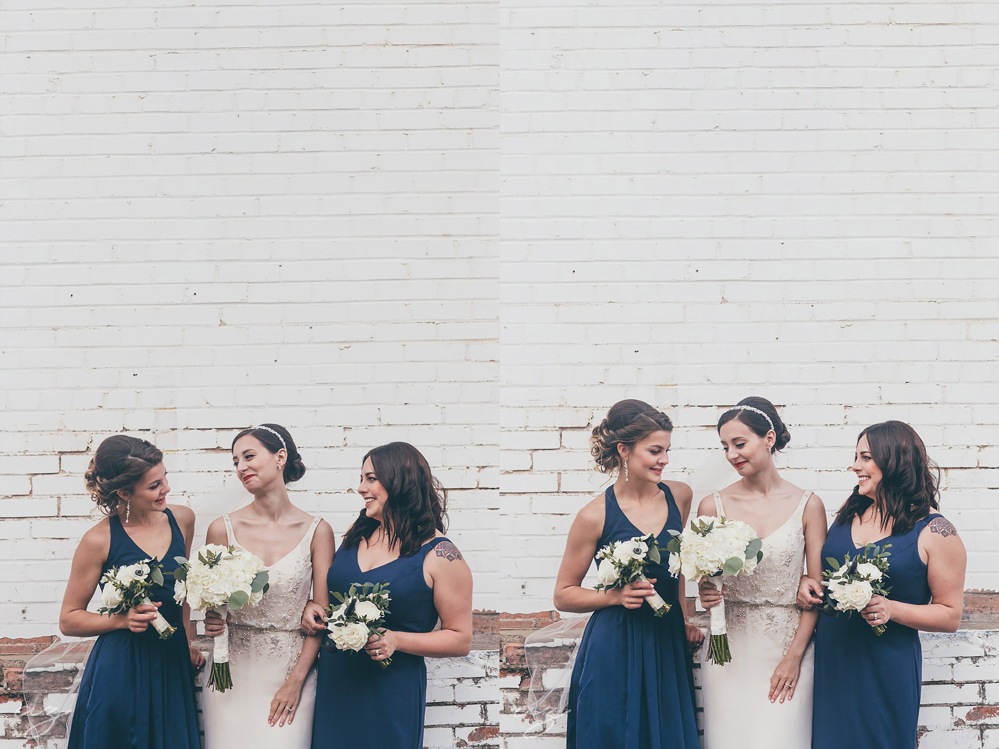 Bride and bridesmaids with navy dresses laughing against a whitewashed brick wall