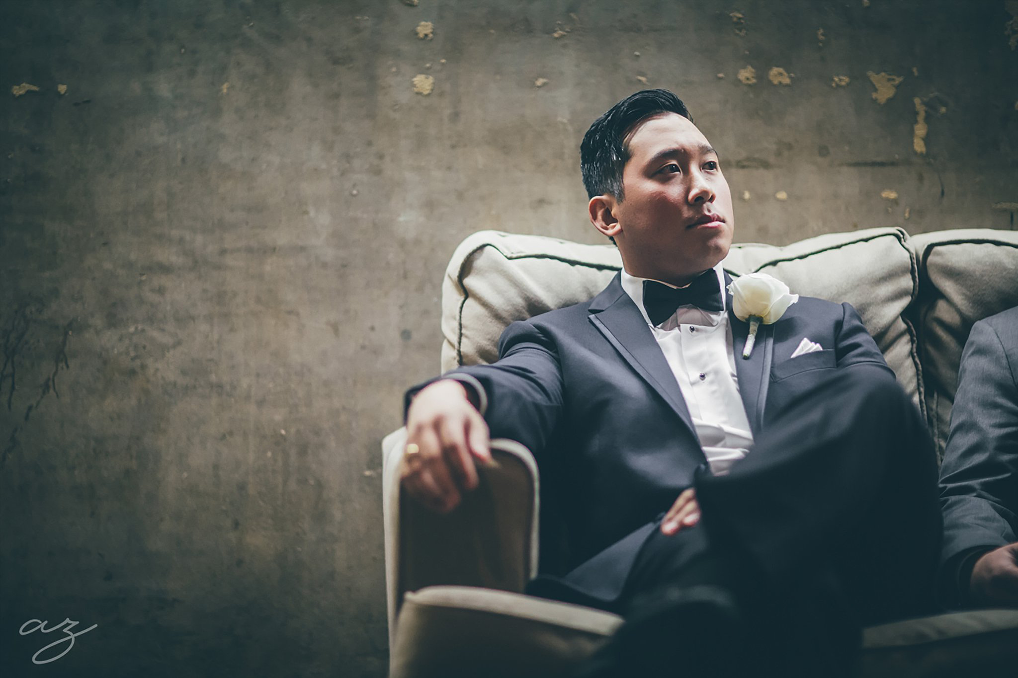 Carlisle Room wedding Groom sitting on tan chair in grey suite with a navy bowtie