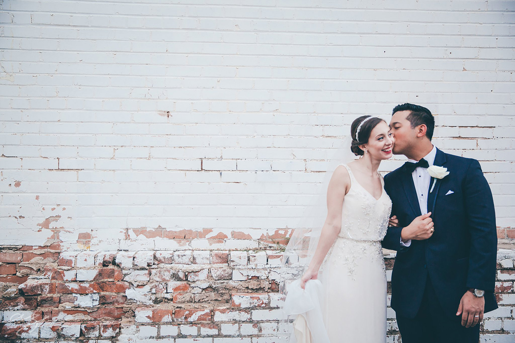 Bride and groom kissing again a whitewashed brick wall