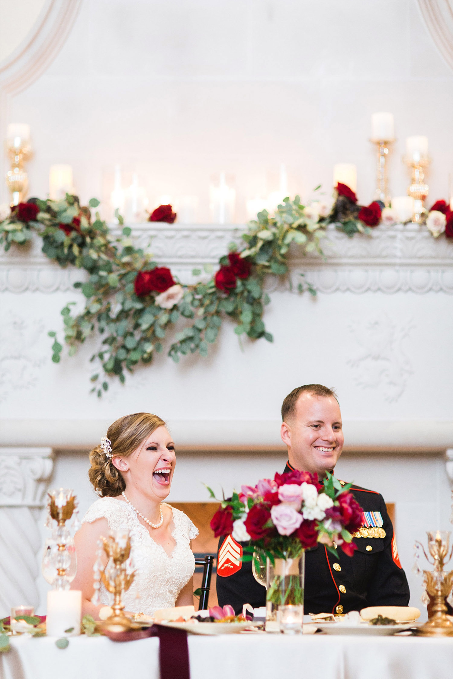 Castle at Rockwall wedding bride and marine groom sitting at sweet heart table in front of fireplace with garland