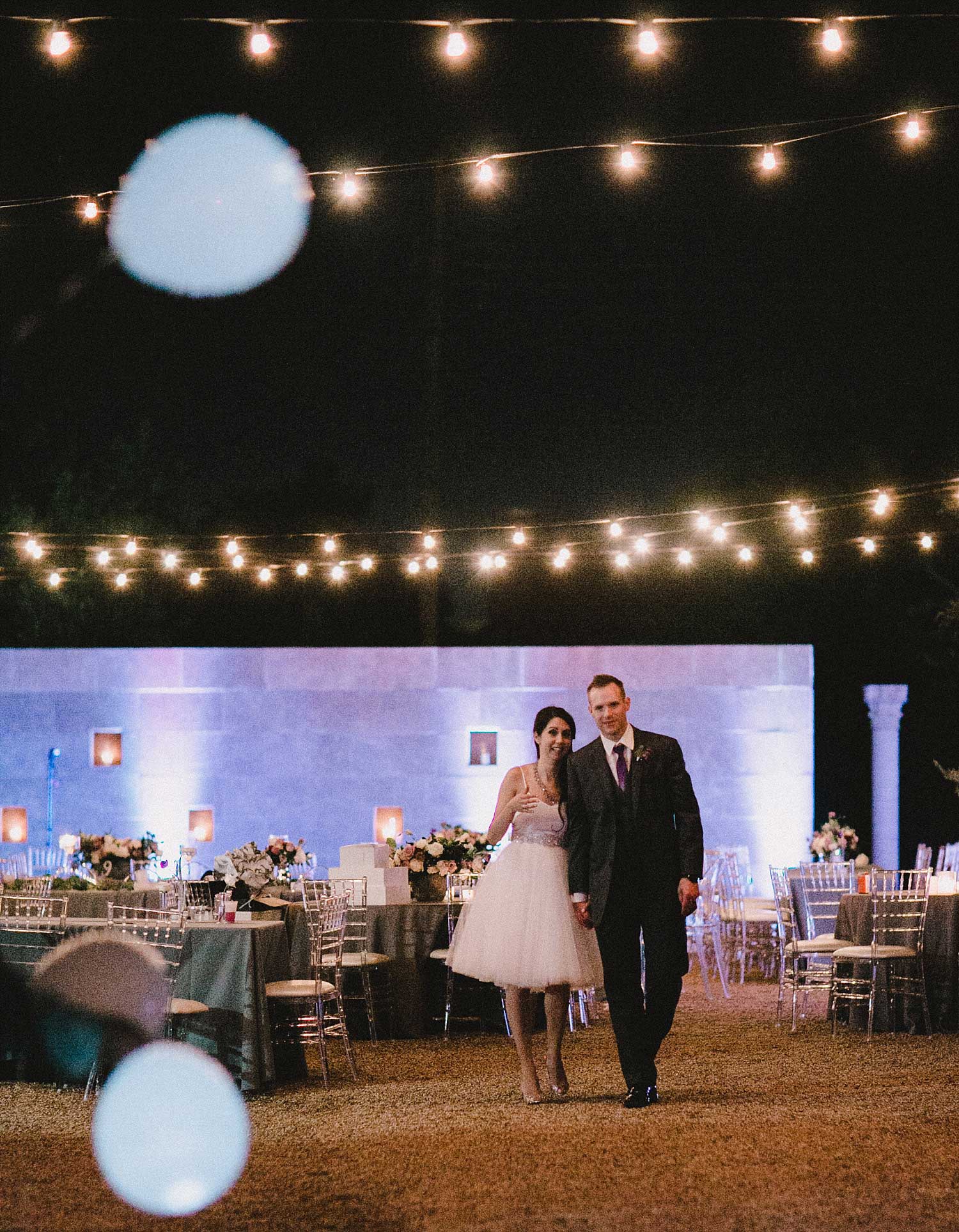 Bride in short dress next to groom with cafe lights
