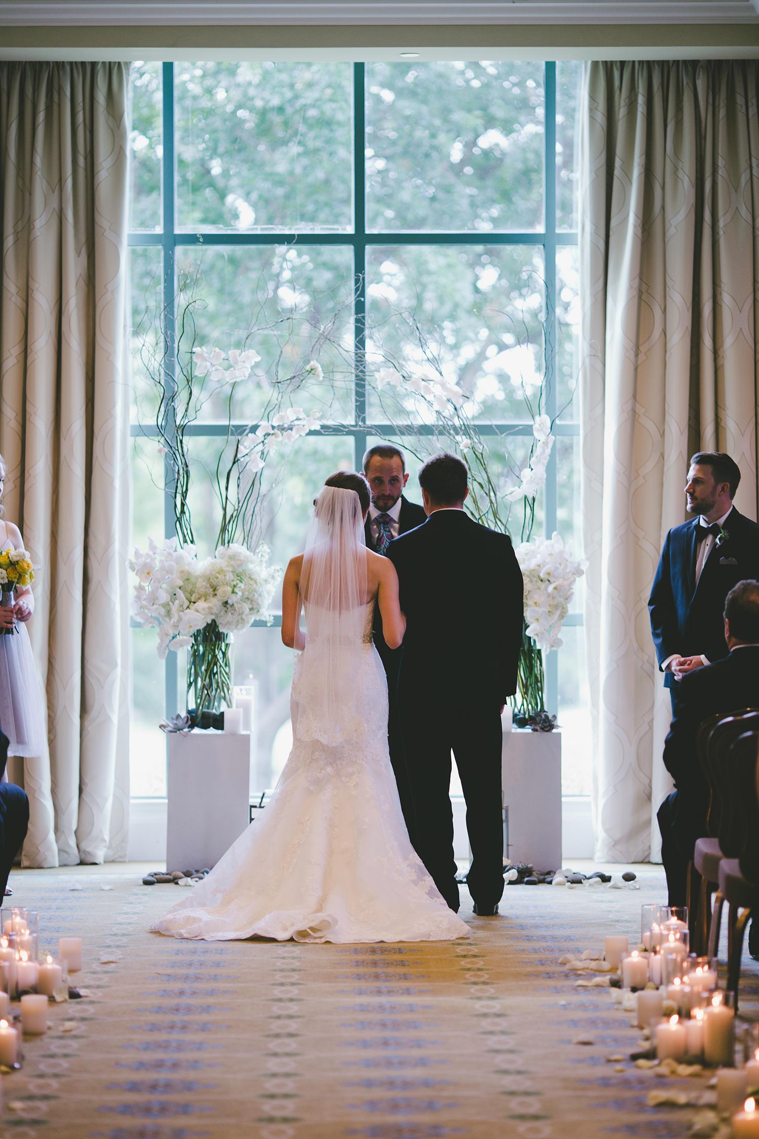 River Crest Country Club ceremony in front of large windows with a white flower and branch archway