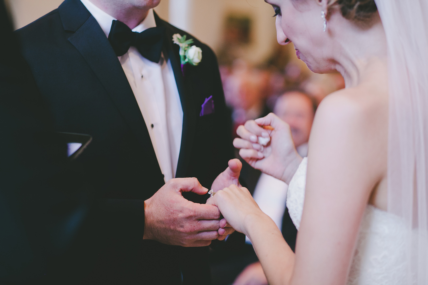 Bride and groom with lavender boutonniere holding hands at ceremony 