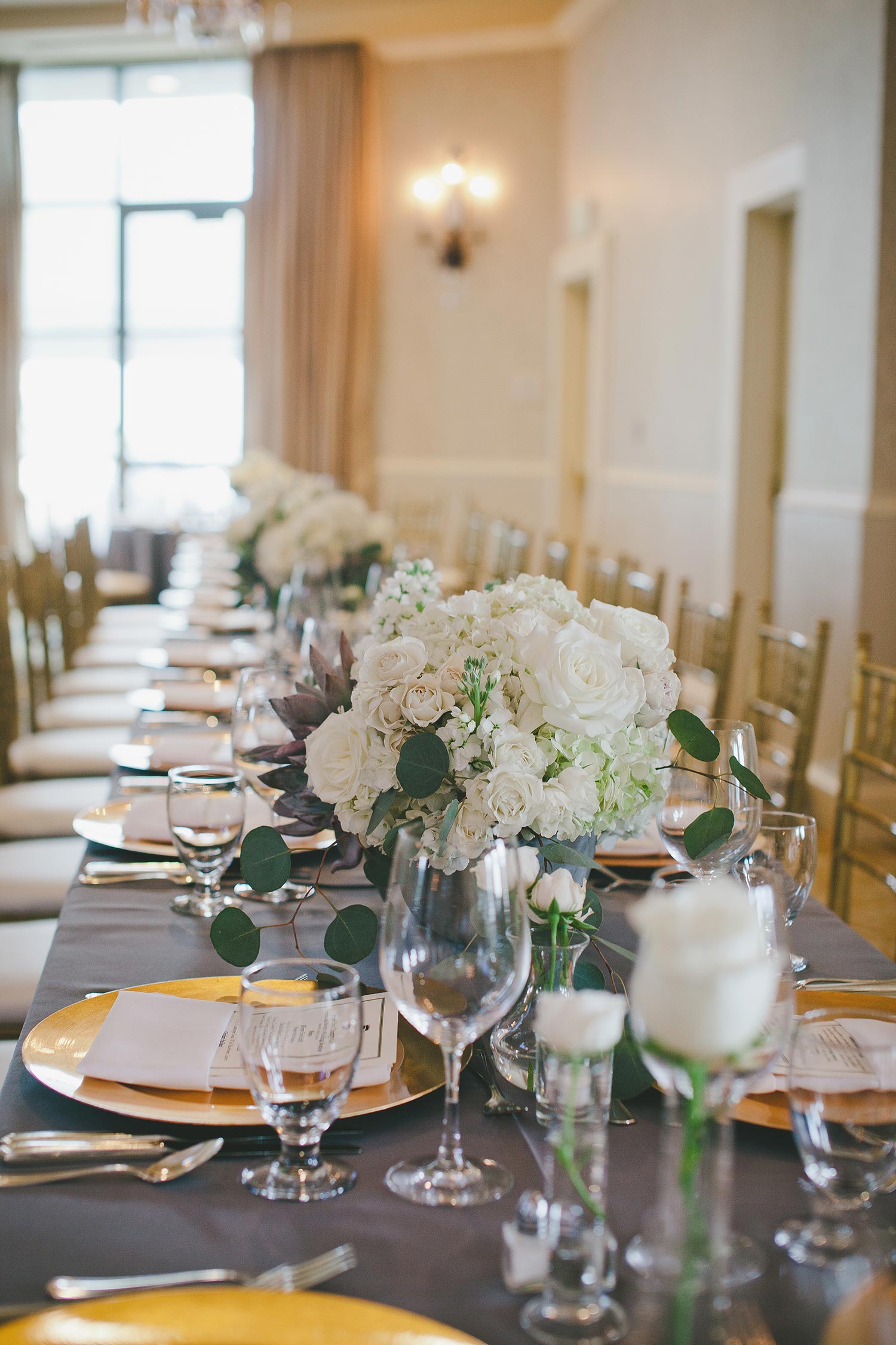 Grey linen table with white flower centerpieces and gold chargers