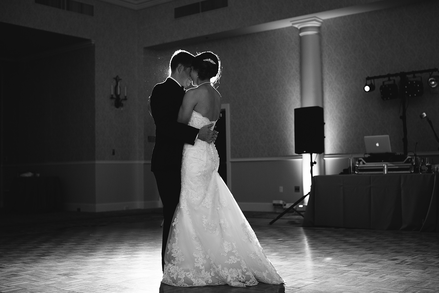 Black and white picture of bride and groom dancing with uplights in the background