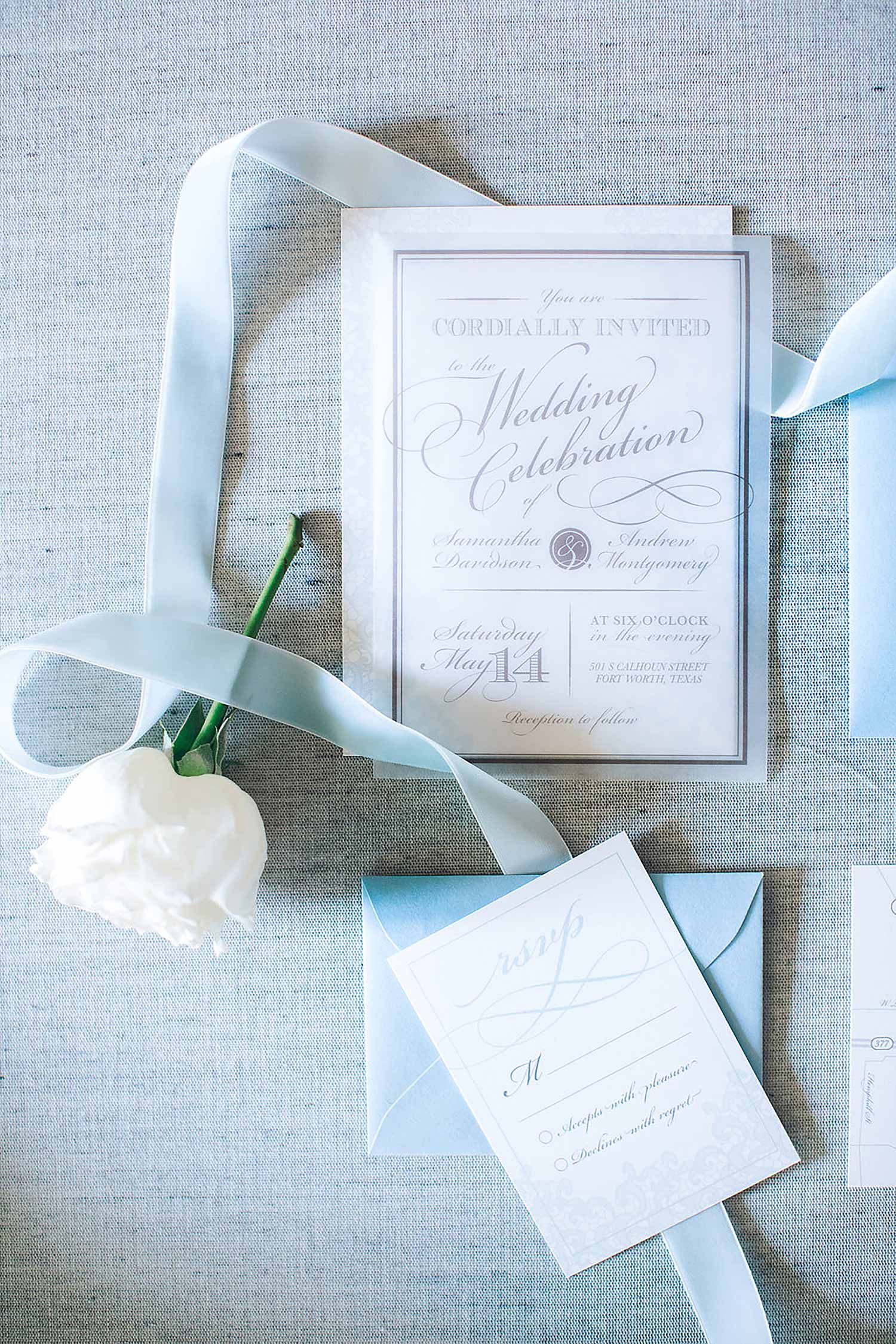 Acrylic wedding inviation and dusty blue envelope with a white rose