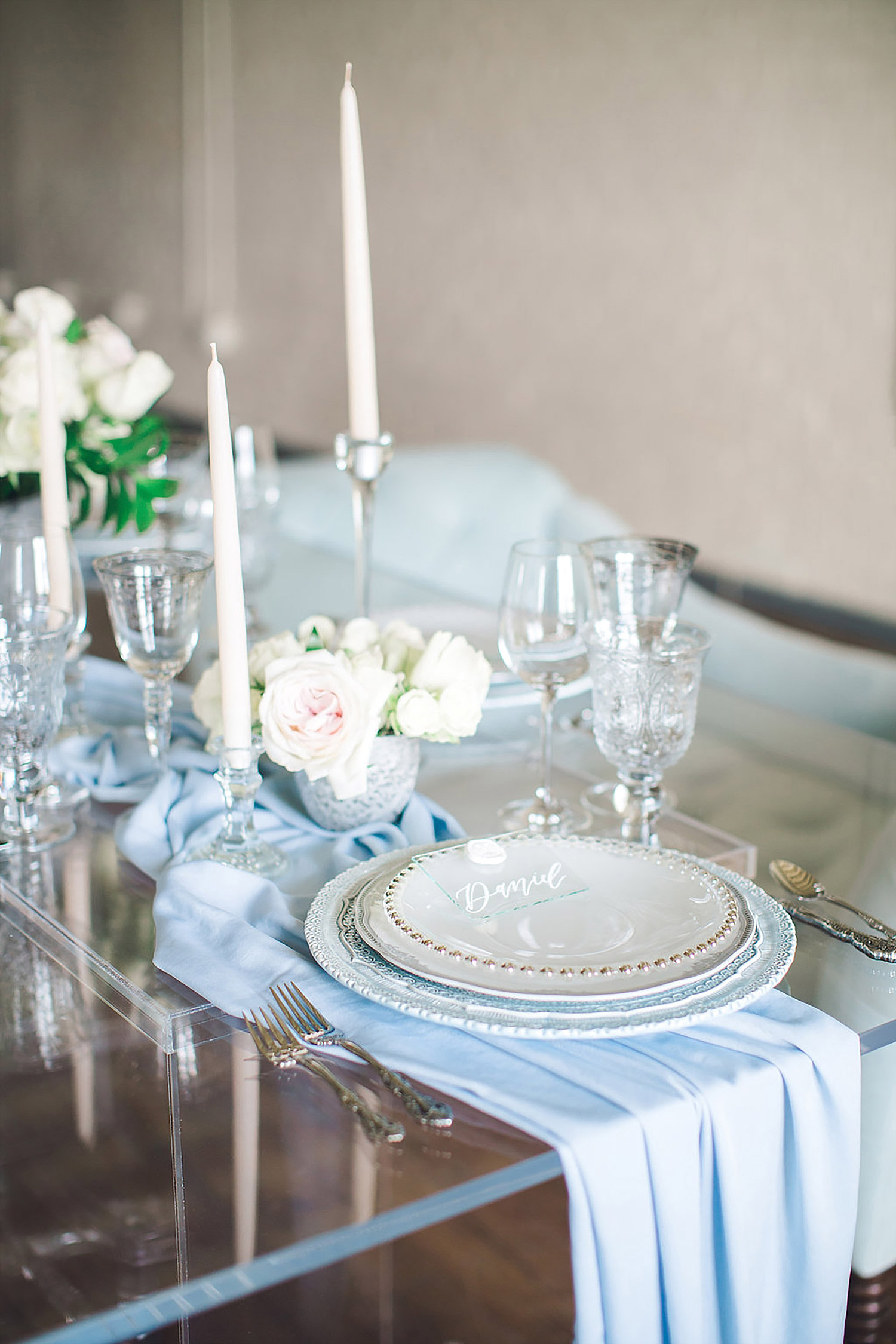 A acrylic table with a dusty blue china charger and tapered candles at Brik Venue