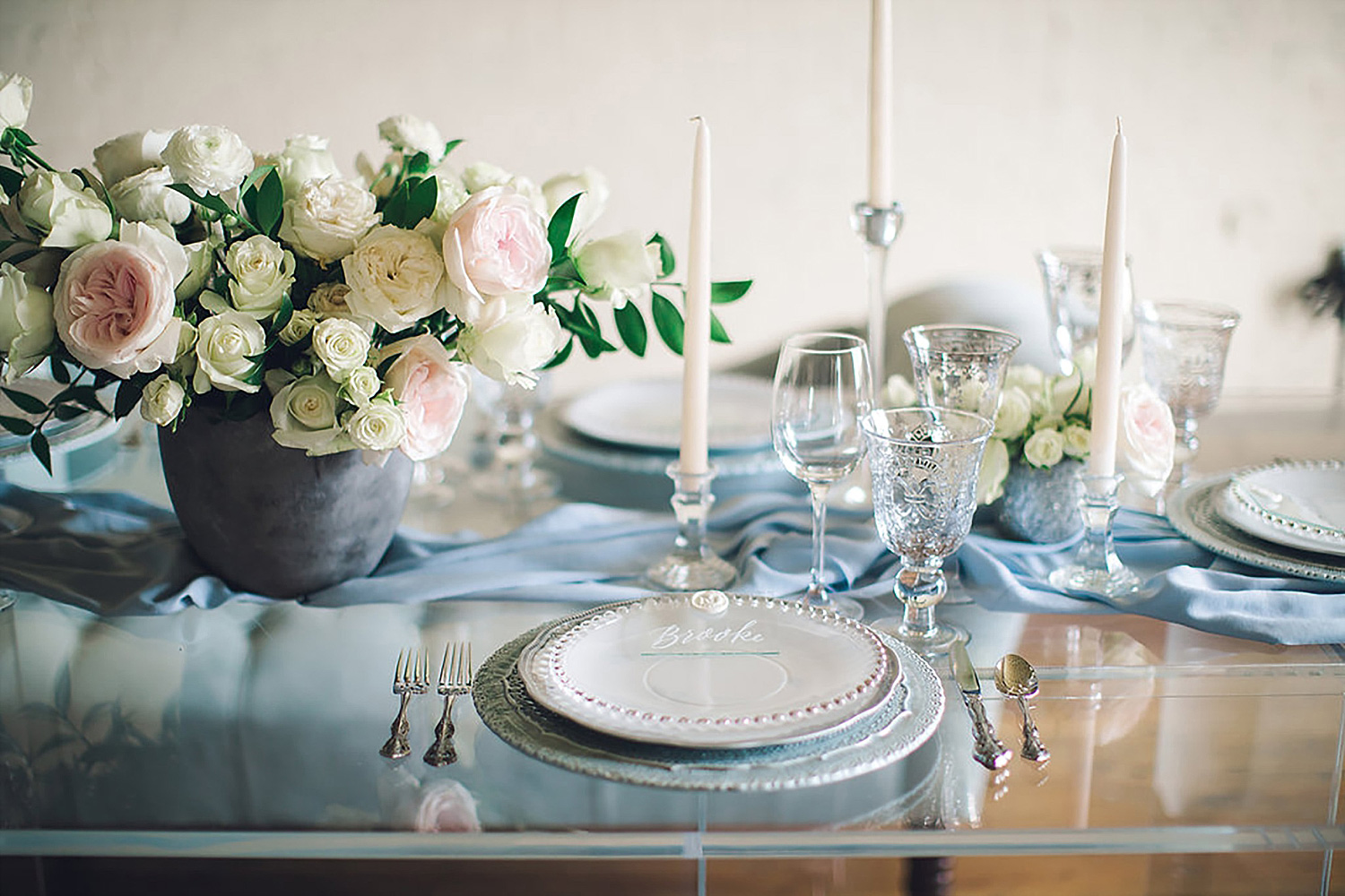 Dusty blue and white place setting with white tapered candles and white and blush flowers
