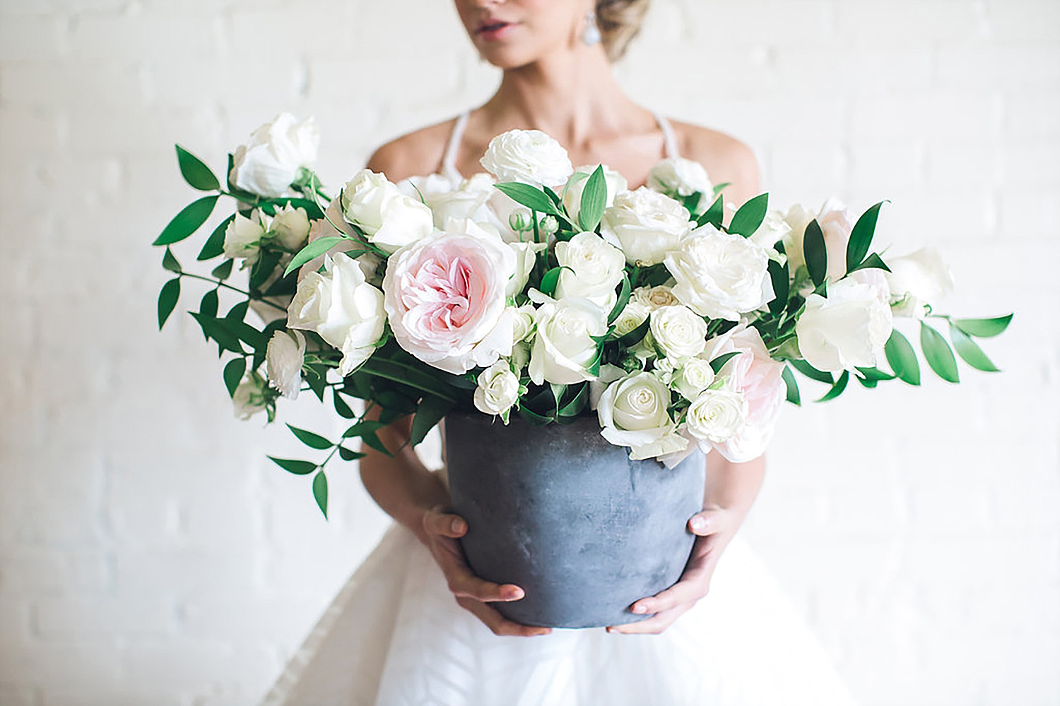 Bride holding white and blush flowers in a concrete vase