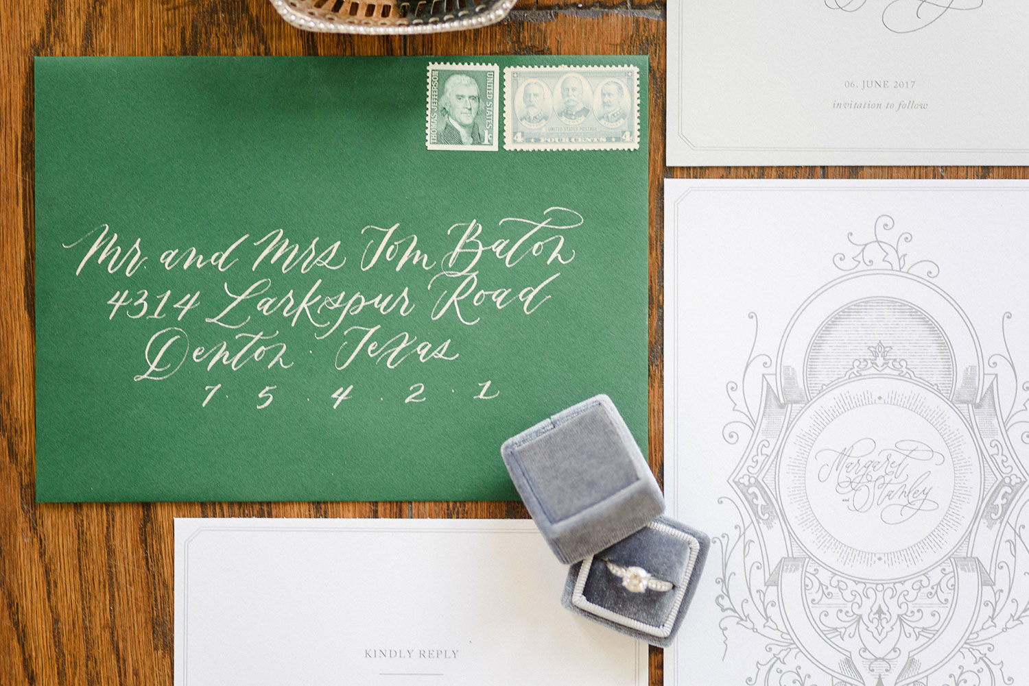 Green envelope wedding invitation with white calligraphy and a light grey velvet ring box