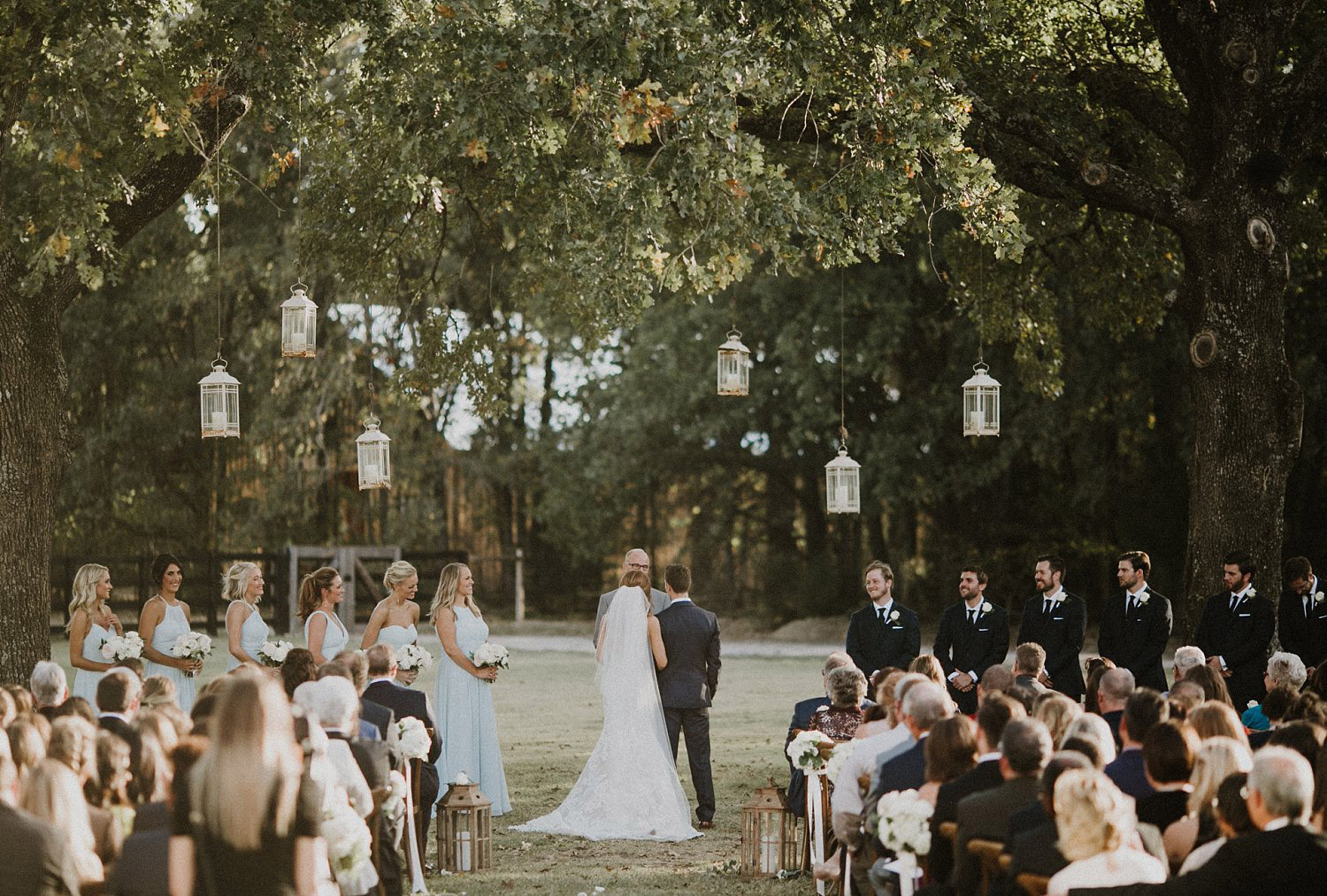 White Sparrow Barn outdoor ceremony with hanging white lanterns with dusty blue bridesmaid dresses