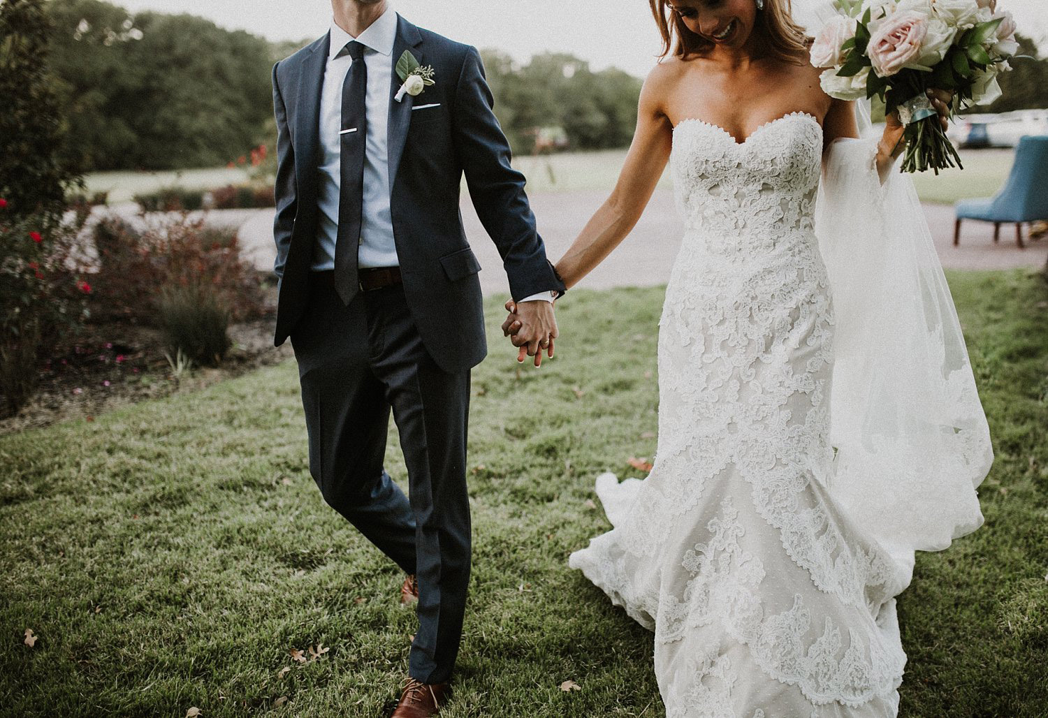 Bride in lace wedding dress holding hand of groom with dark grey suite and tie