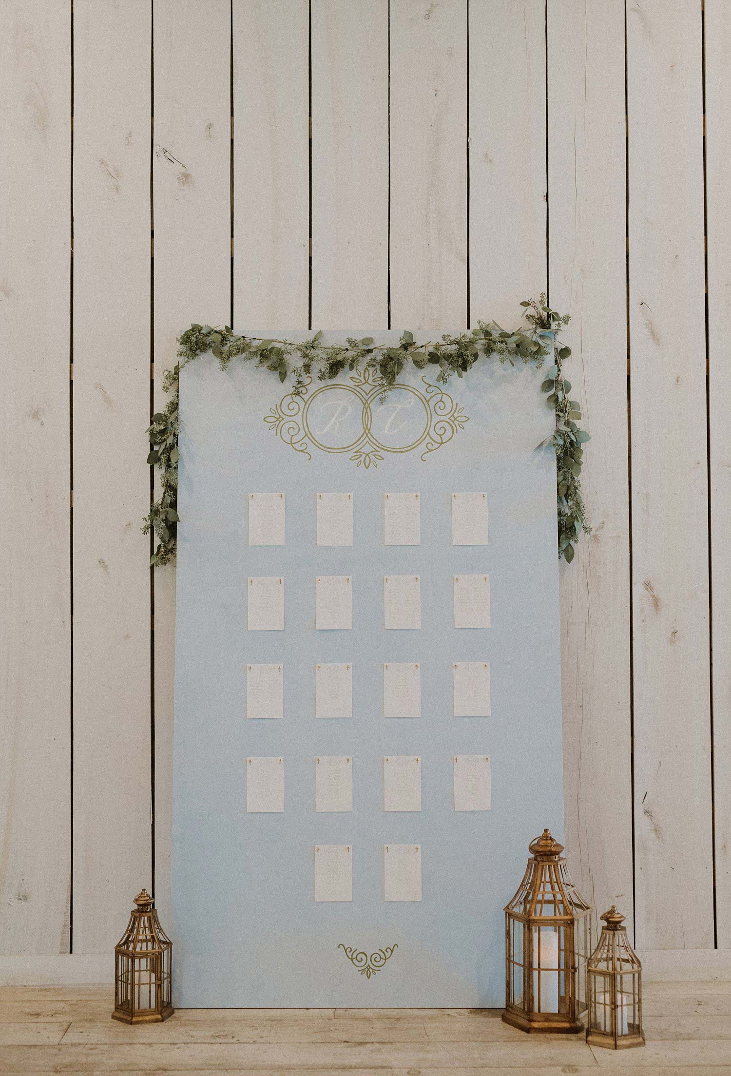 DIY dusty blue seating chart with gold lanterns and gold monogram at White Sparrow Barn