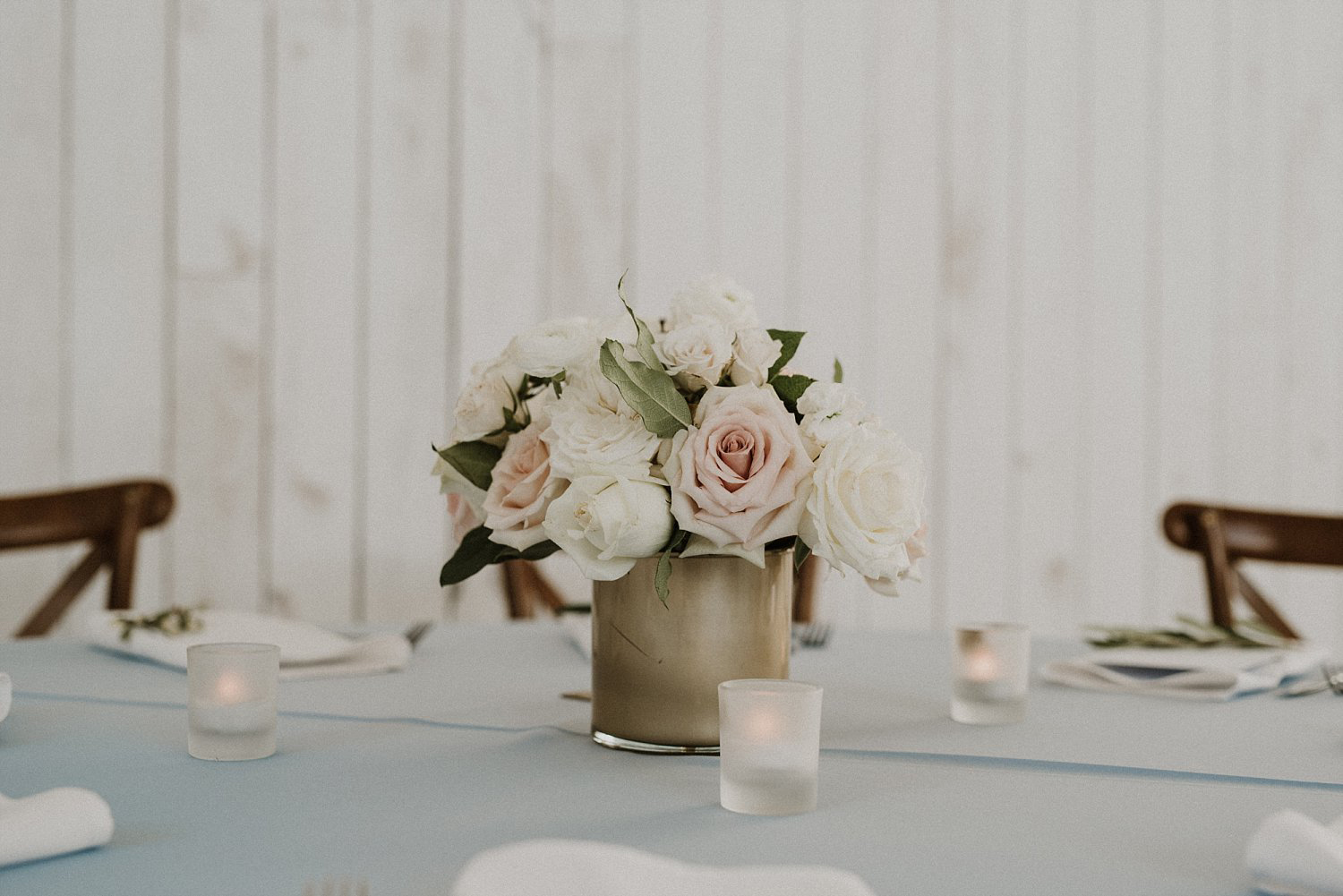 Simple white and blush flower arrangement in a gold vase on a light blue linen