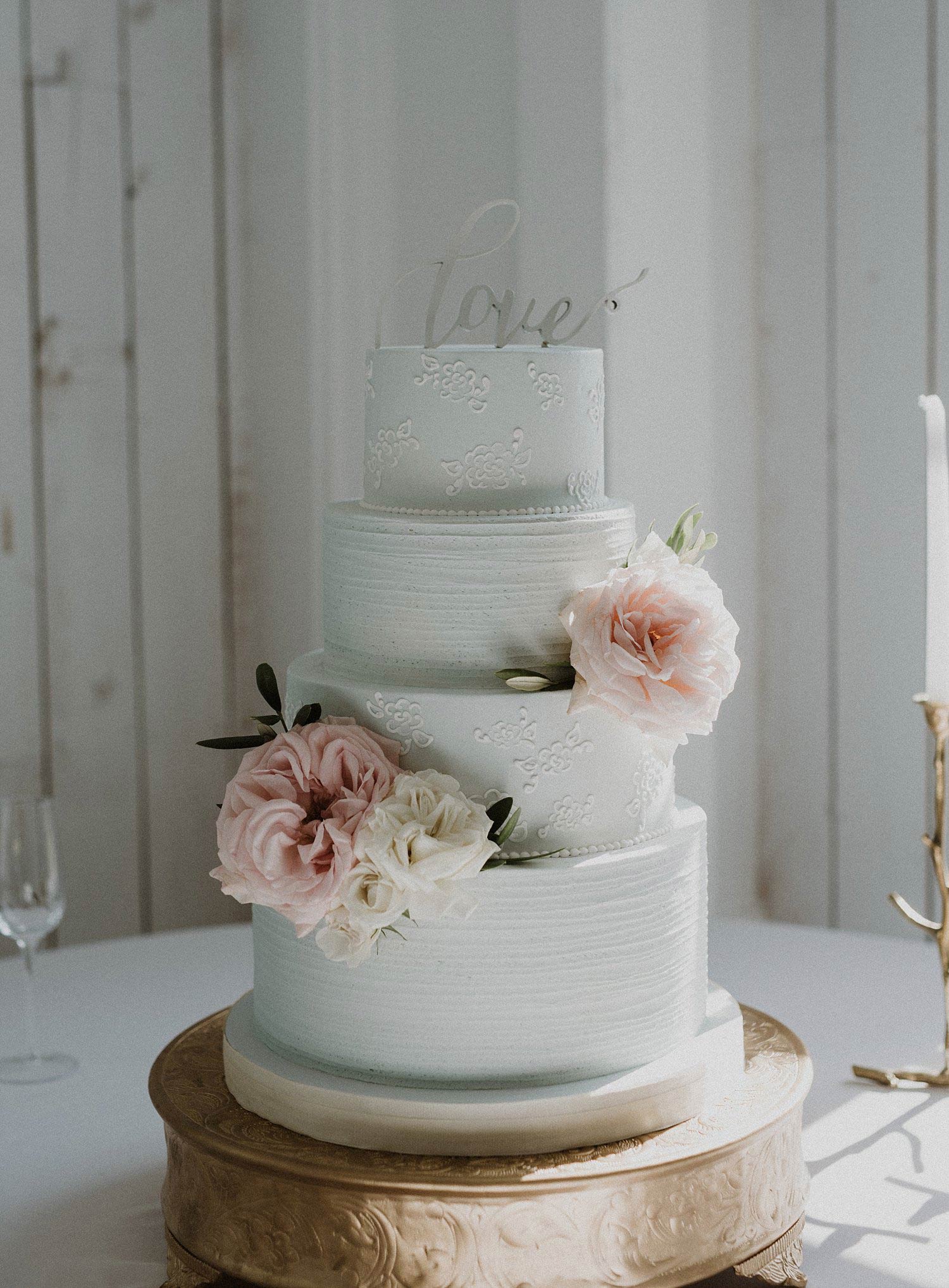 Light blue wedding cake with white lace pattern on gold cake stand