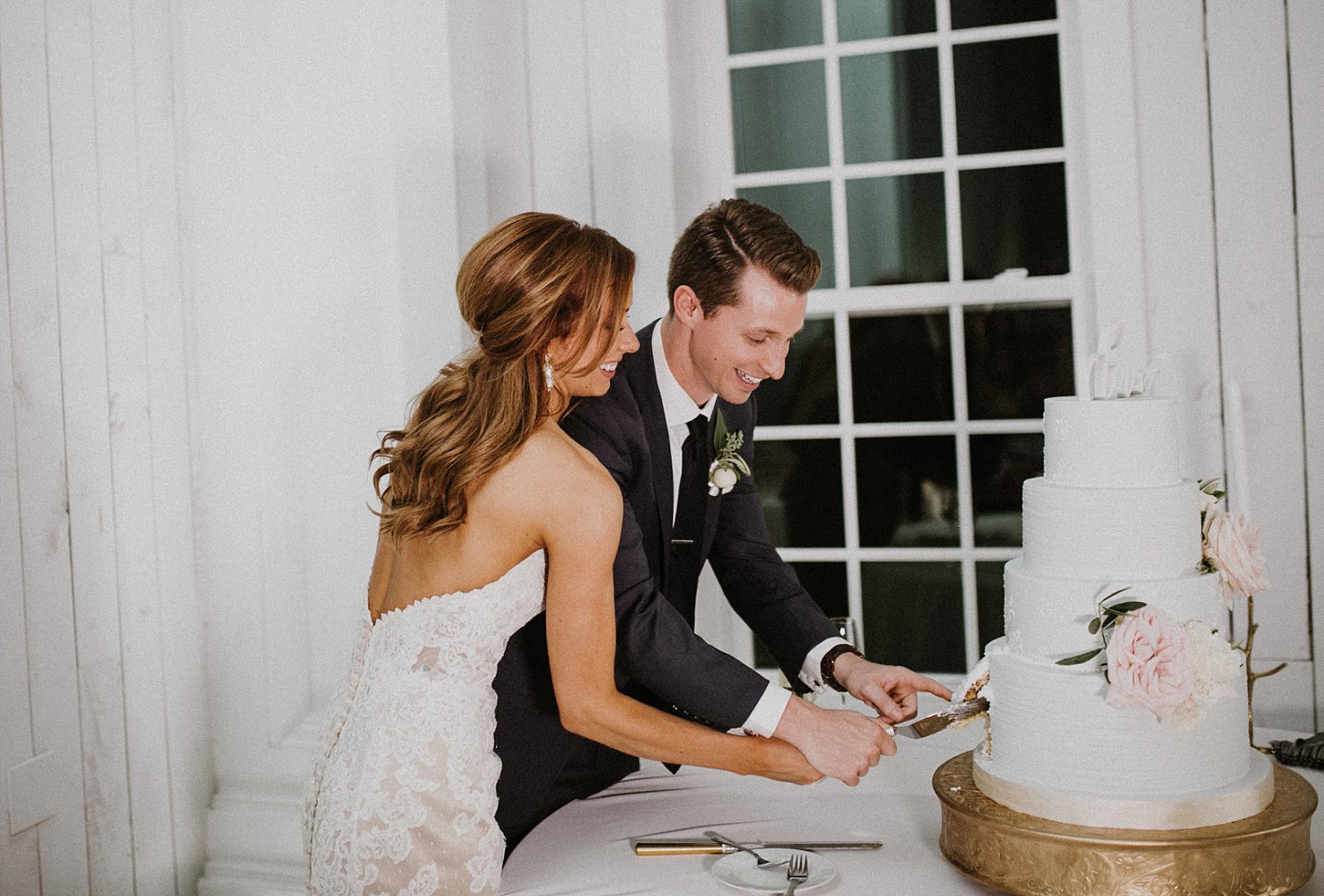 Bride and groom cutting wedding cake in front of white and white shiplap wall