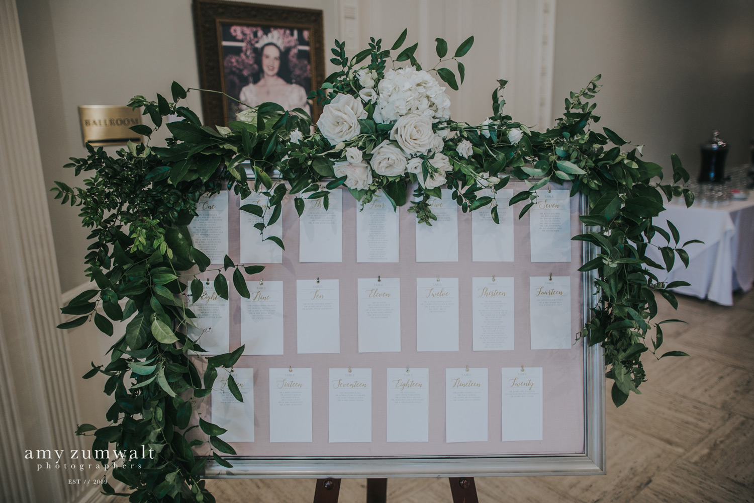 Gold frame seating chart with blush backing, gold frame, and white and green garland
