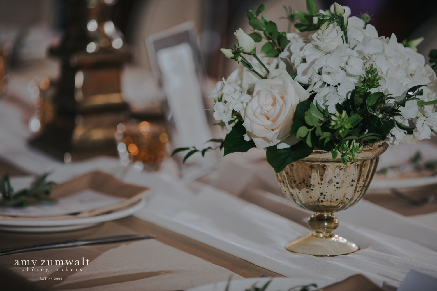 Small flower arrangment in gold urn on white chiffon runner